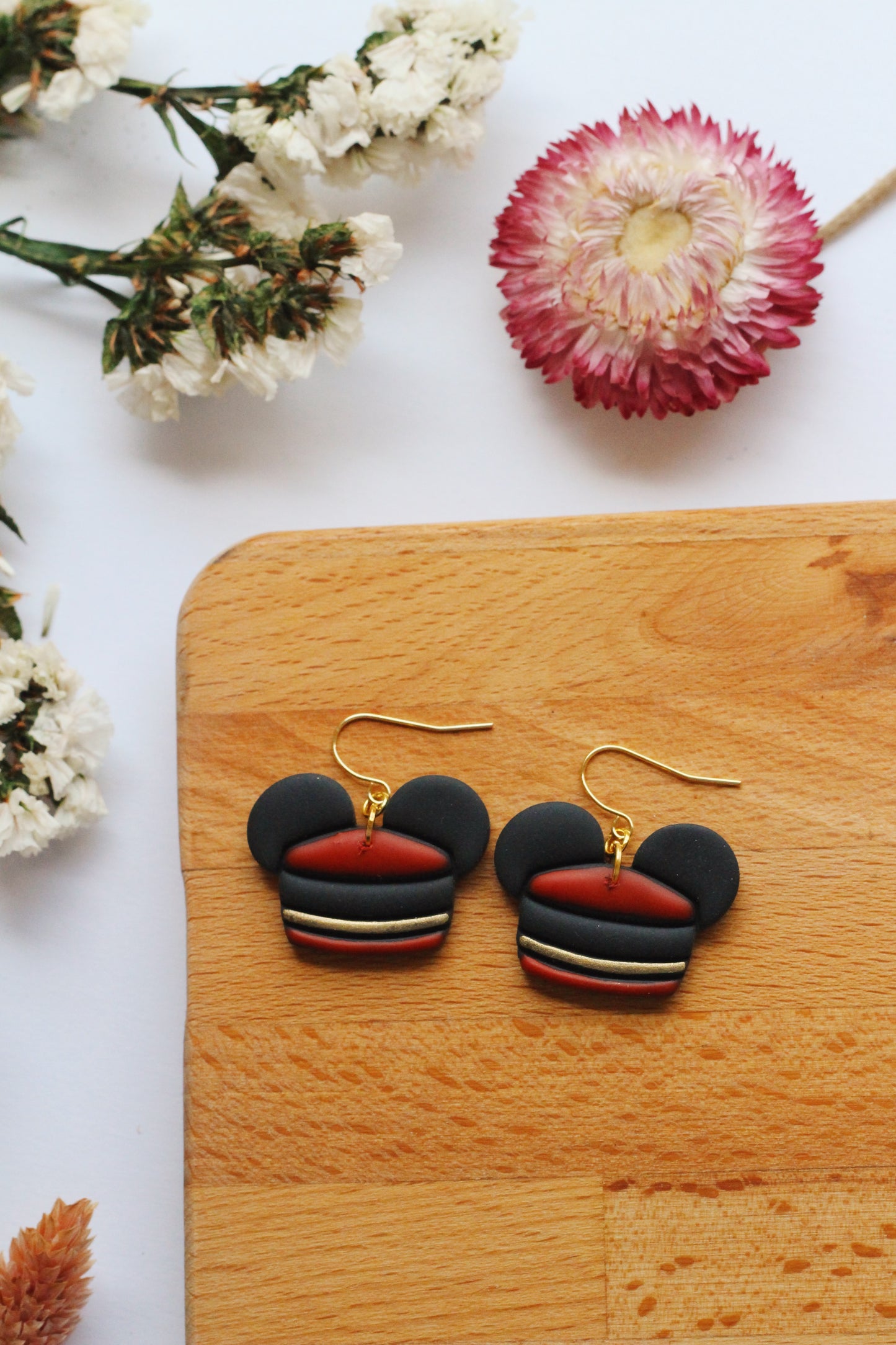 Black and red earrings on a wooden board with flowers in the background