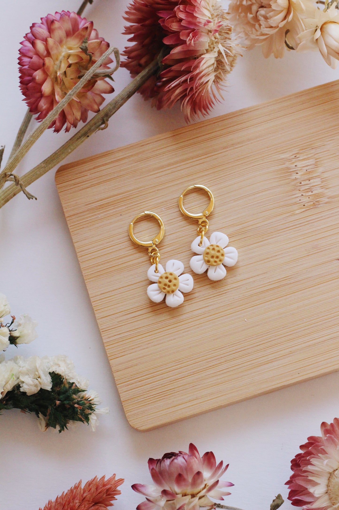 Flower-shaped earrings on a wooden board with floral decorations.