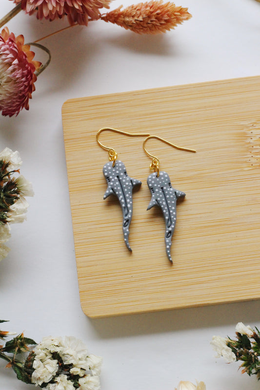Shark-shaped earrings on a wooden board with flowers around