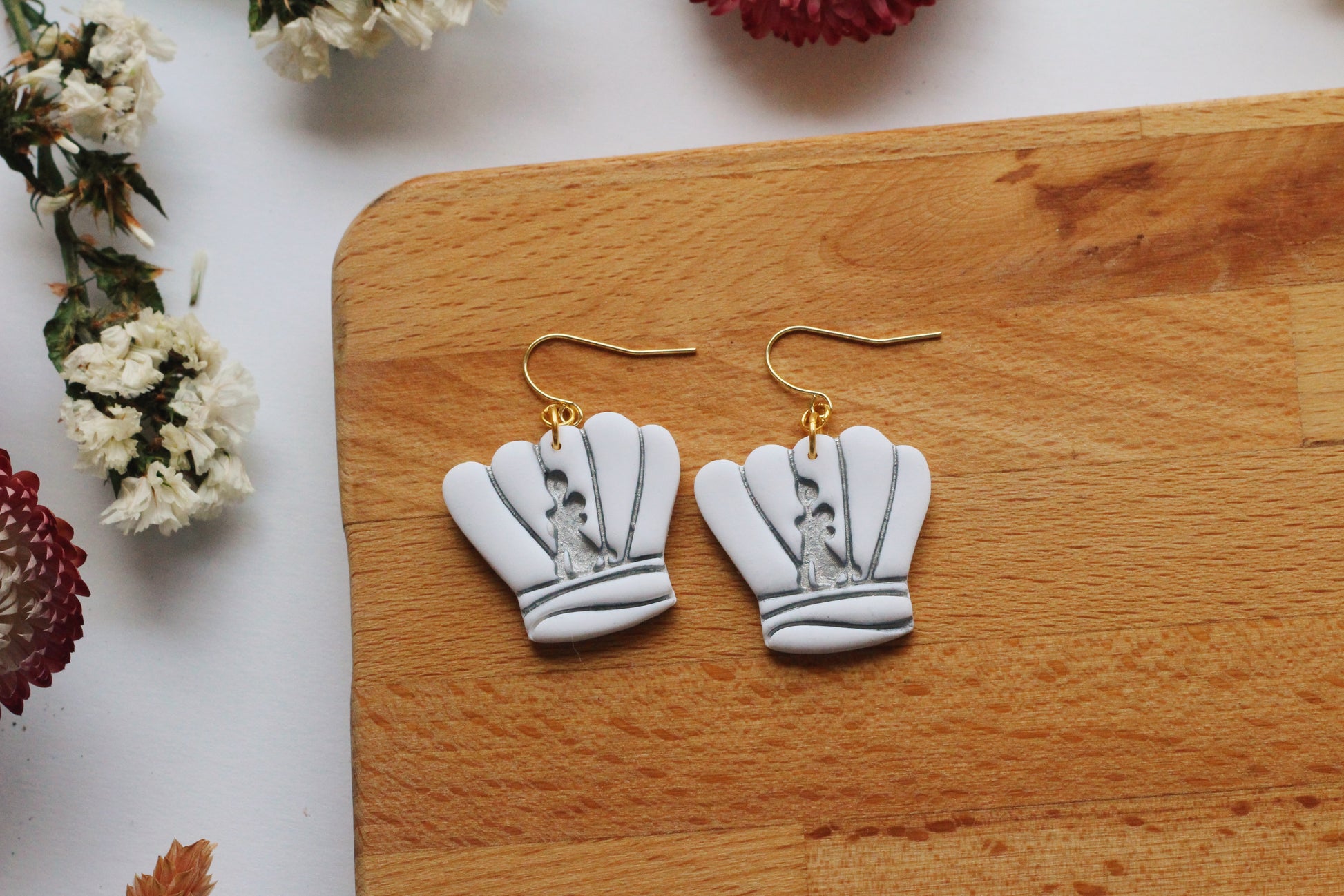 Chef earrings on a wooden board with flowers in the background