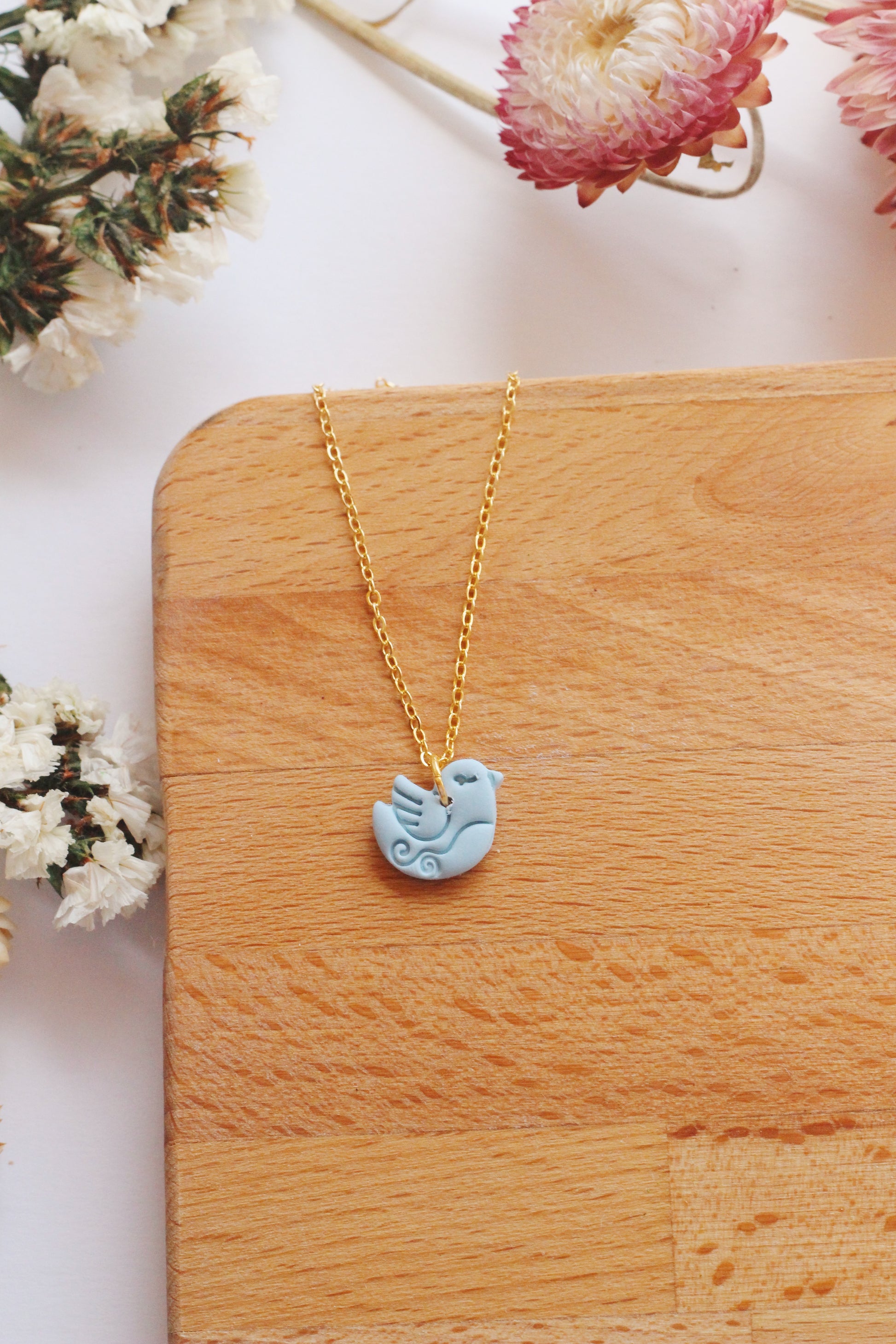 Necklace with a bird pendant on a wooden surface with flowers in the background