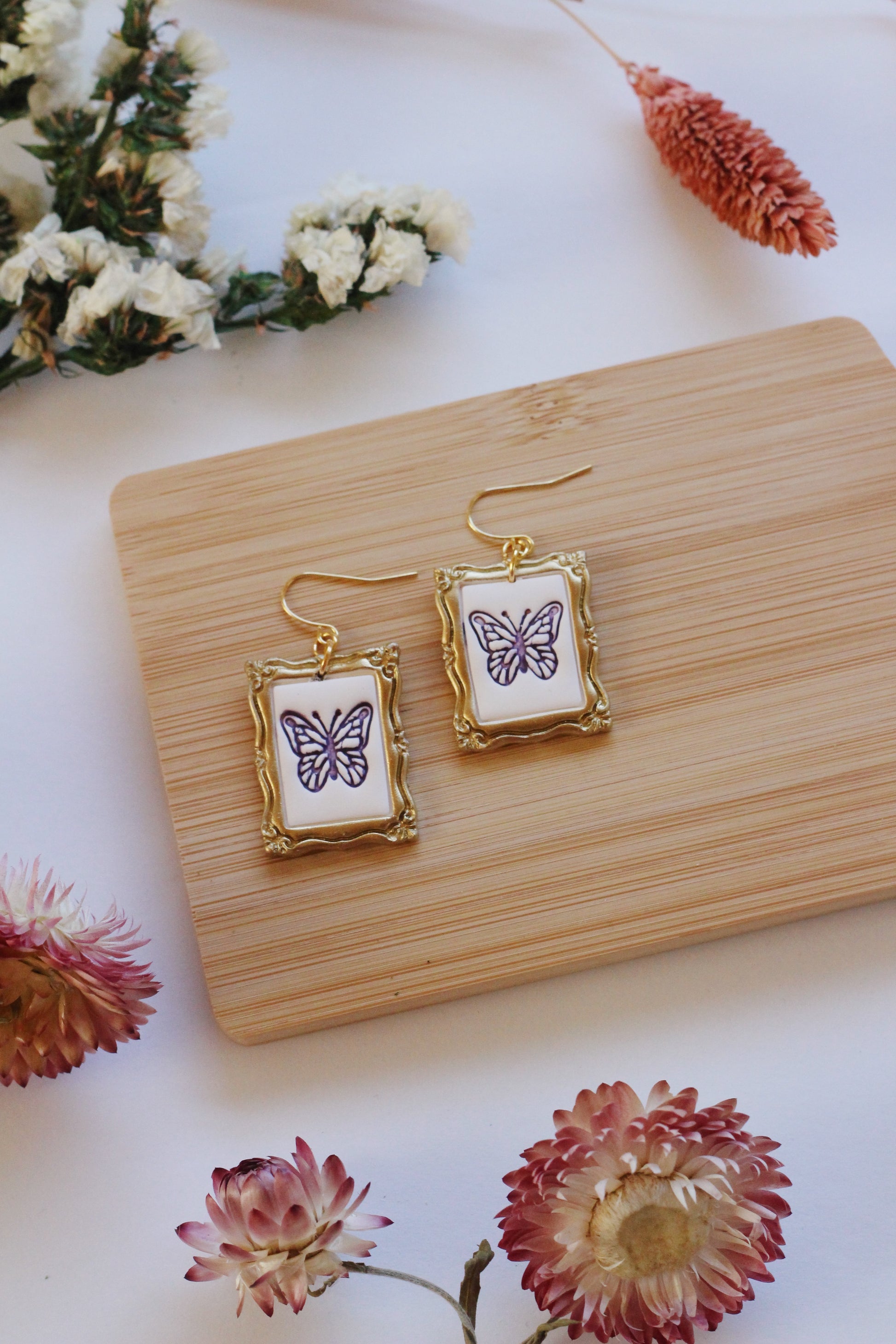 Butterfly-themed earrings on a wooden stand with flowers around