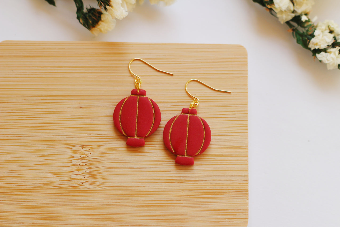 Red lantern-shaped earrings on a wooden board with a light background
