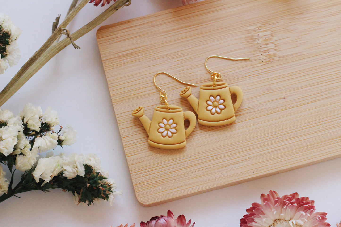 Teapot-shaped earrings on a wooden board with flowers in the background