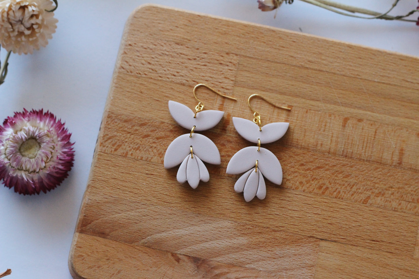 White floral earrings on a wooden board with flowers in the background