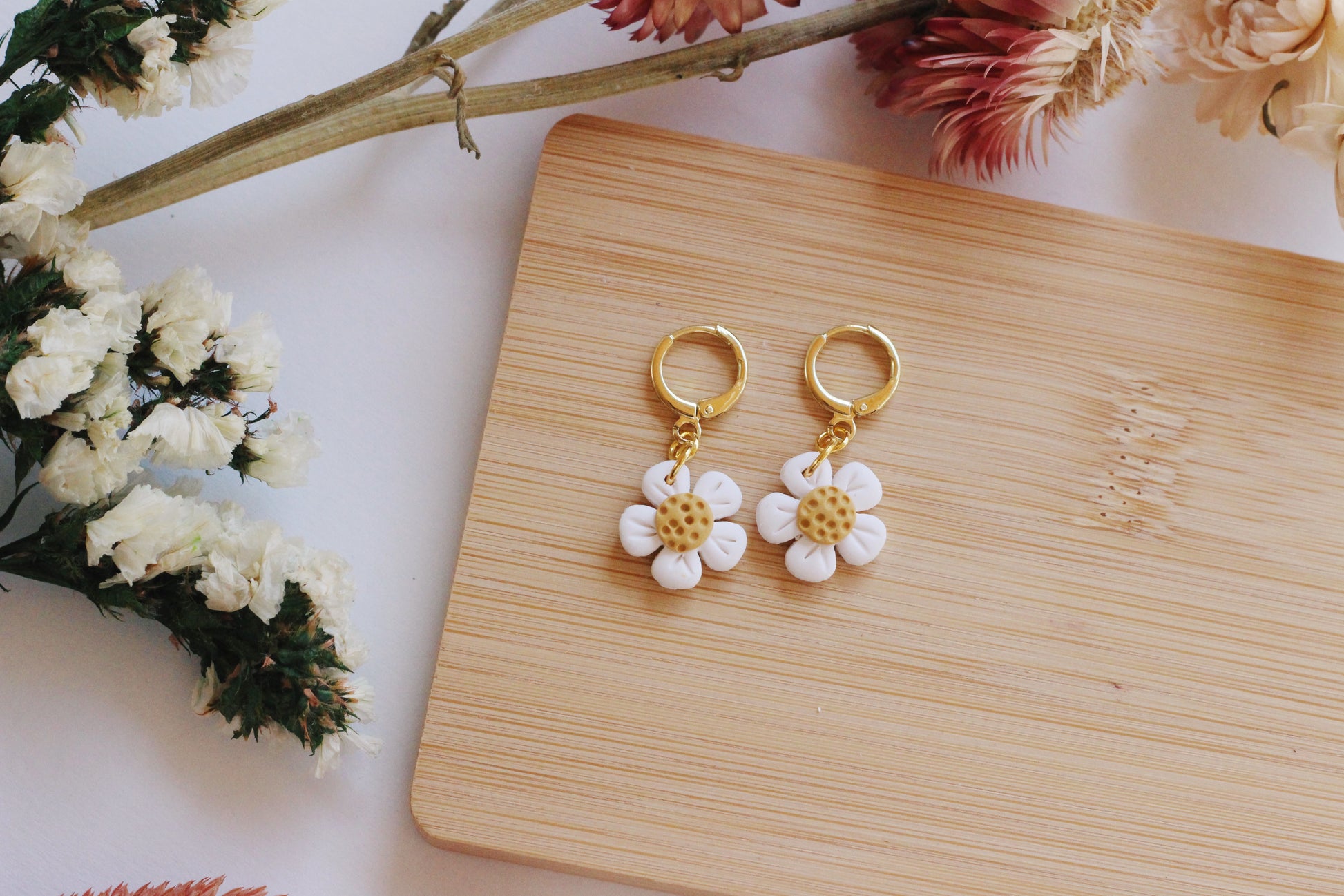 Flower-shaped earrings on a wooden board with floral decorations.