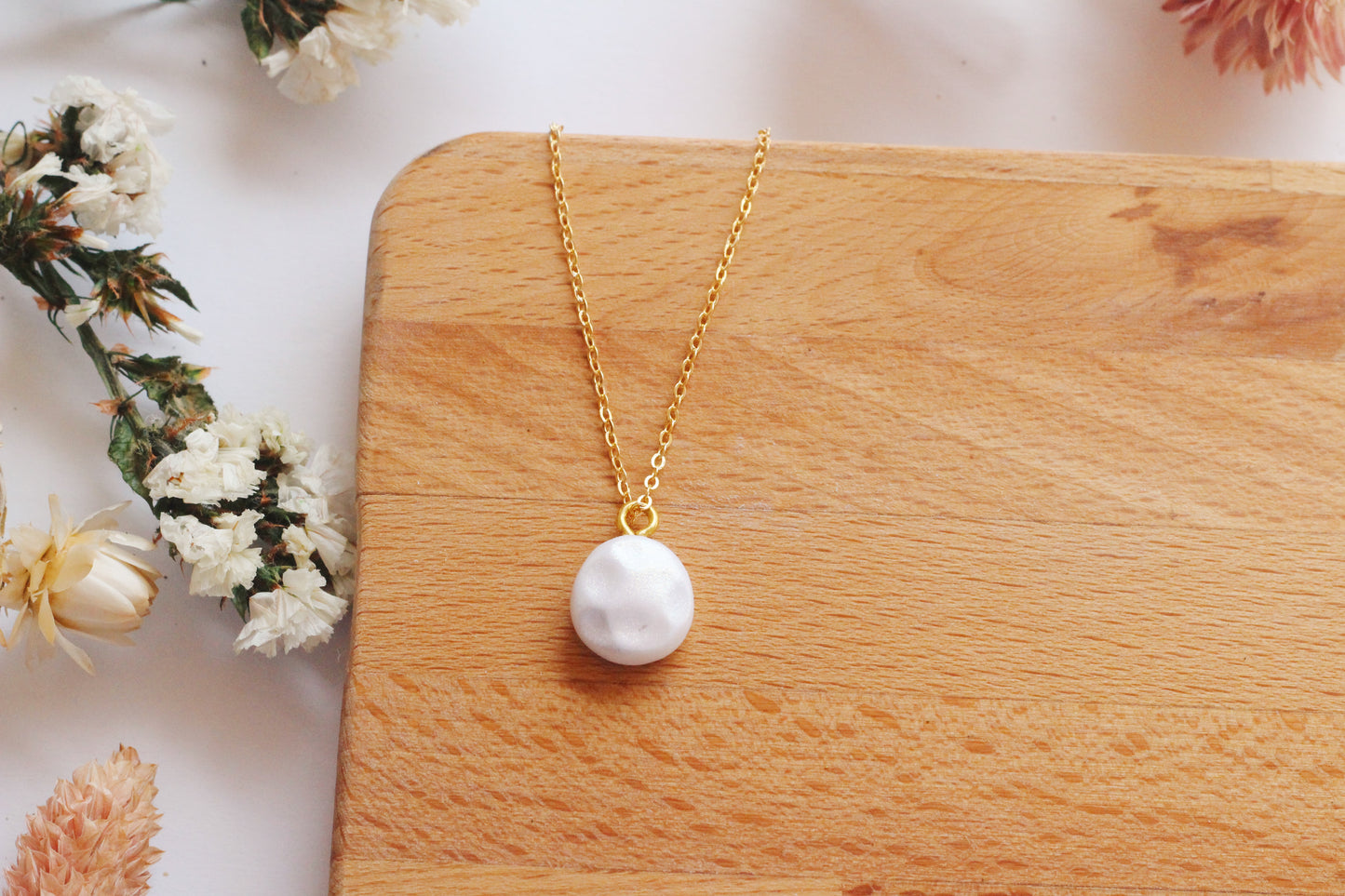 Faux pearl necklace on a wooden surface with flowers in the background