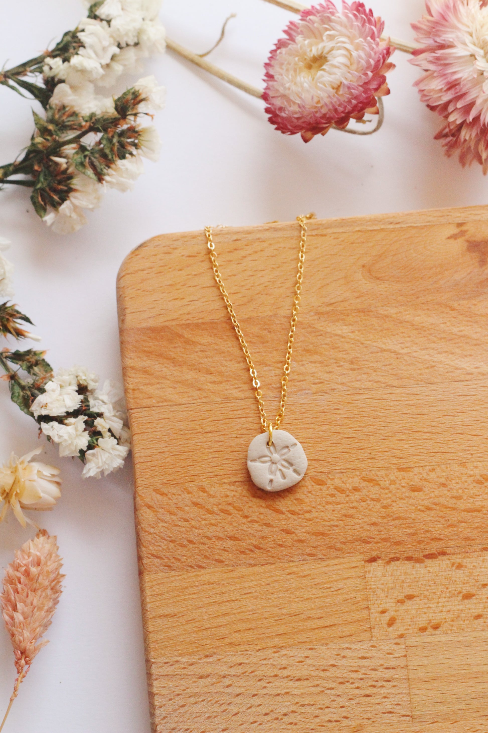 Gold necklace with a sand dollar pendant on a wooden surface with flowers