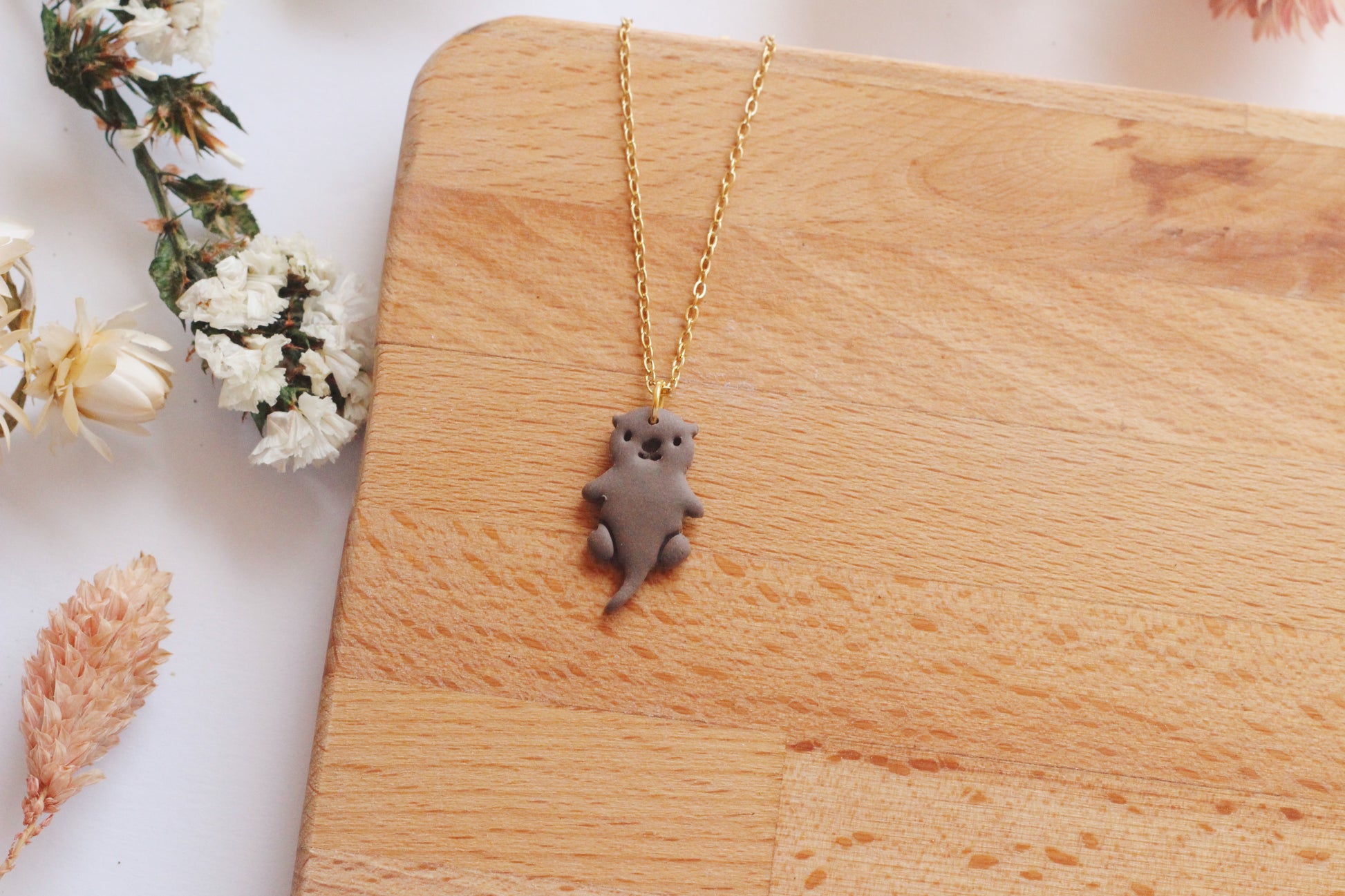 Necklace with an otter pendant on a wooden surface with flowers in the background