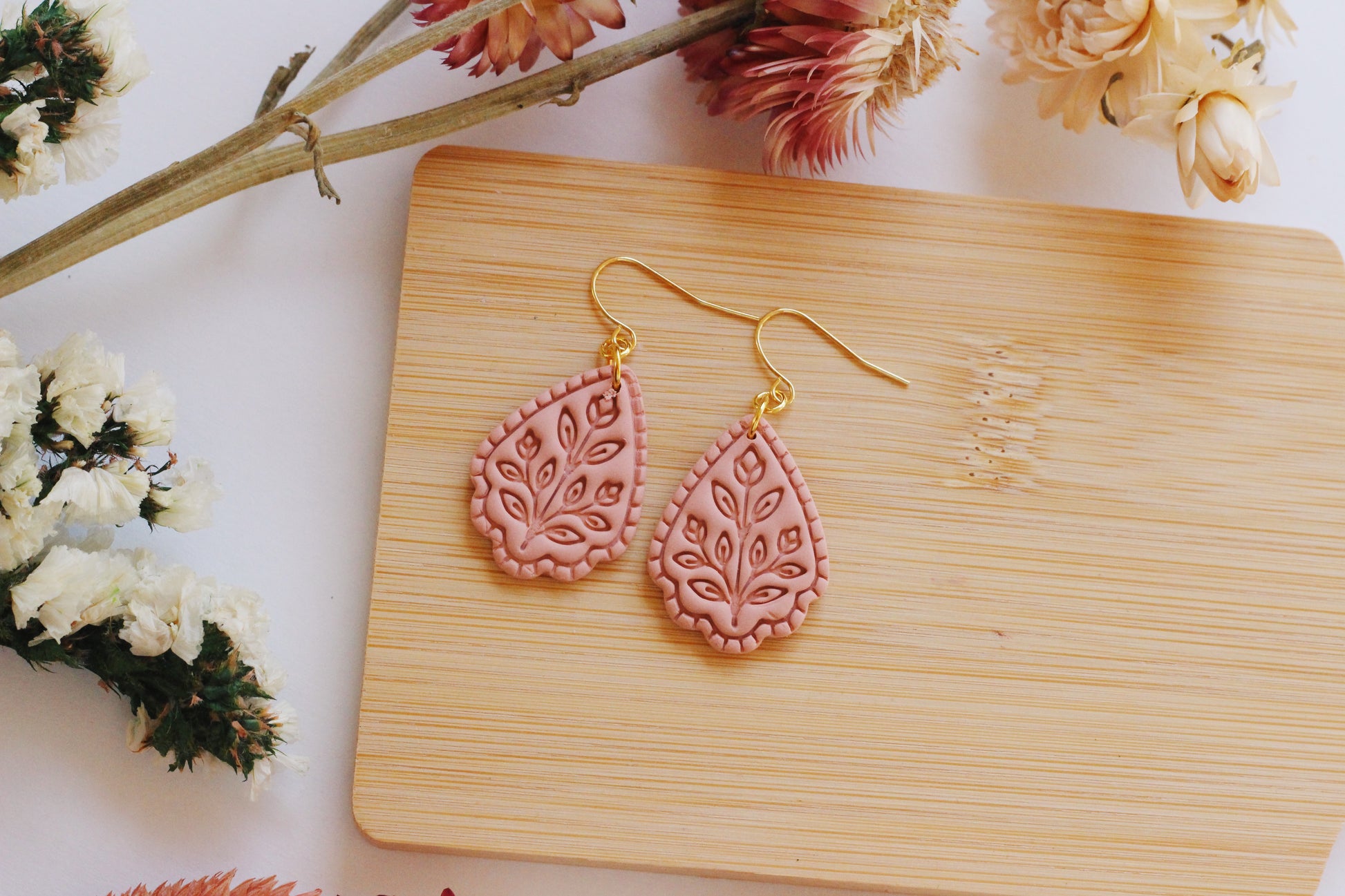 Pink earrings on a wooden board with flowers in the background