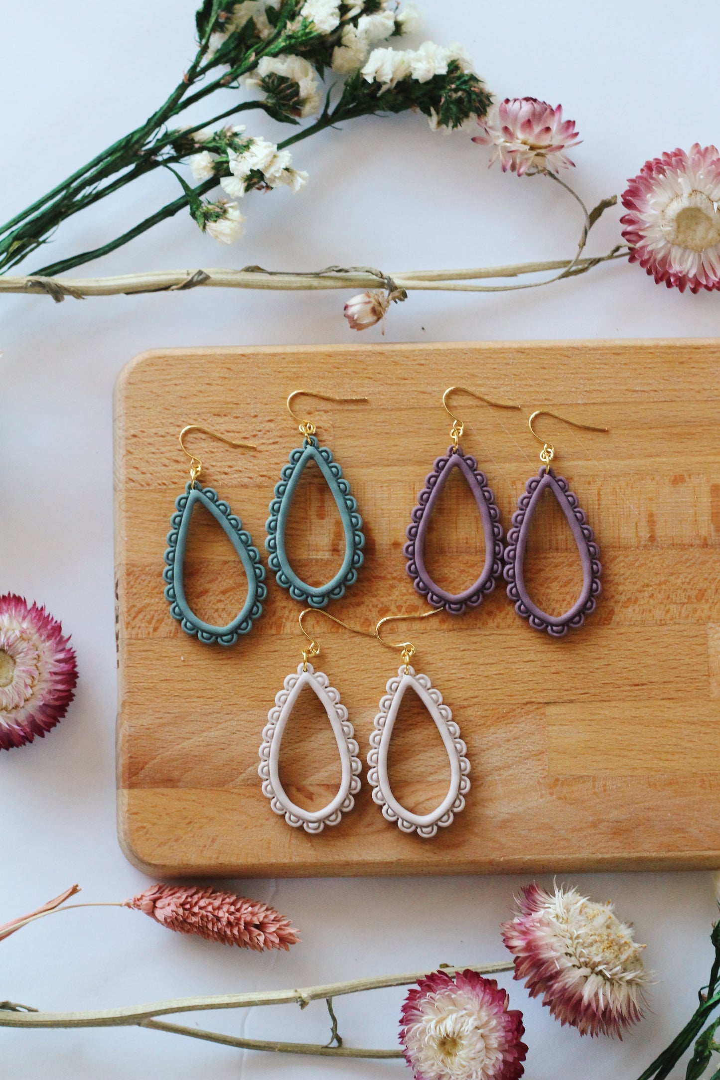 Set of colorful earrings on a wooden board with flowers around