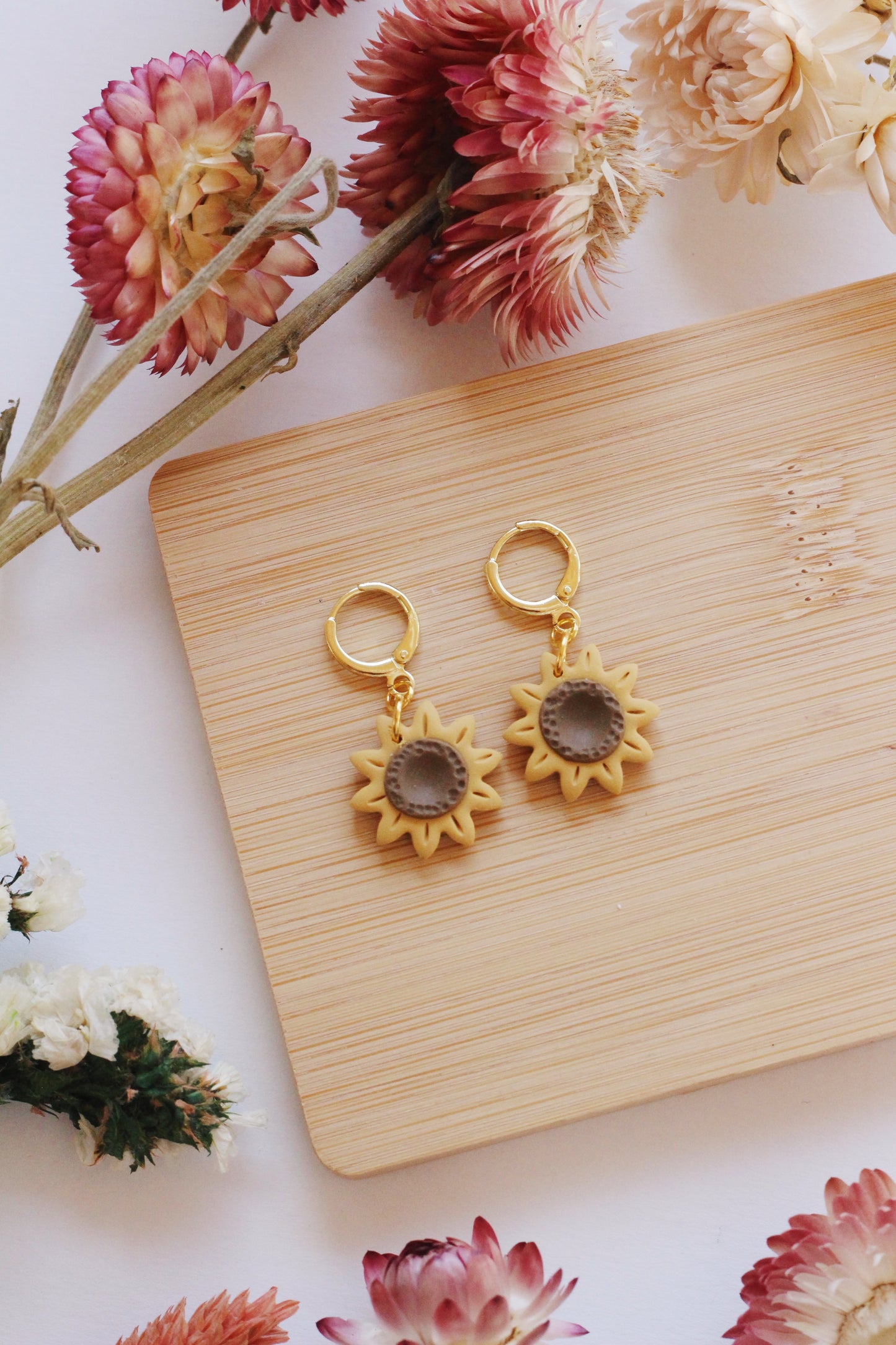 Sunflower-shaped earrings on a wooden board with flowers around