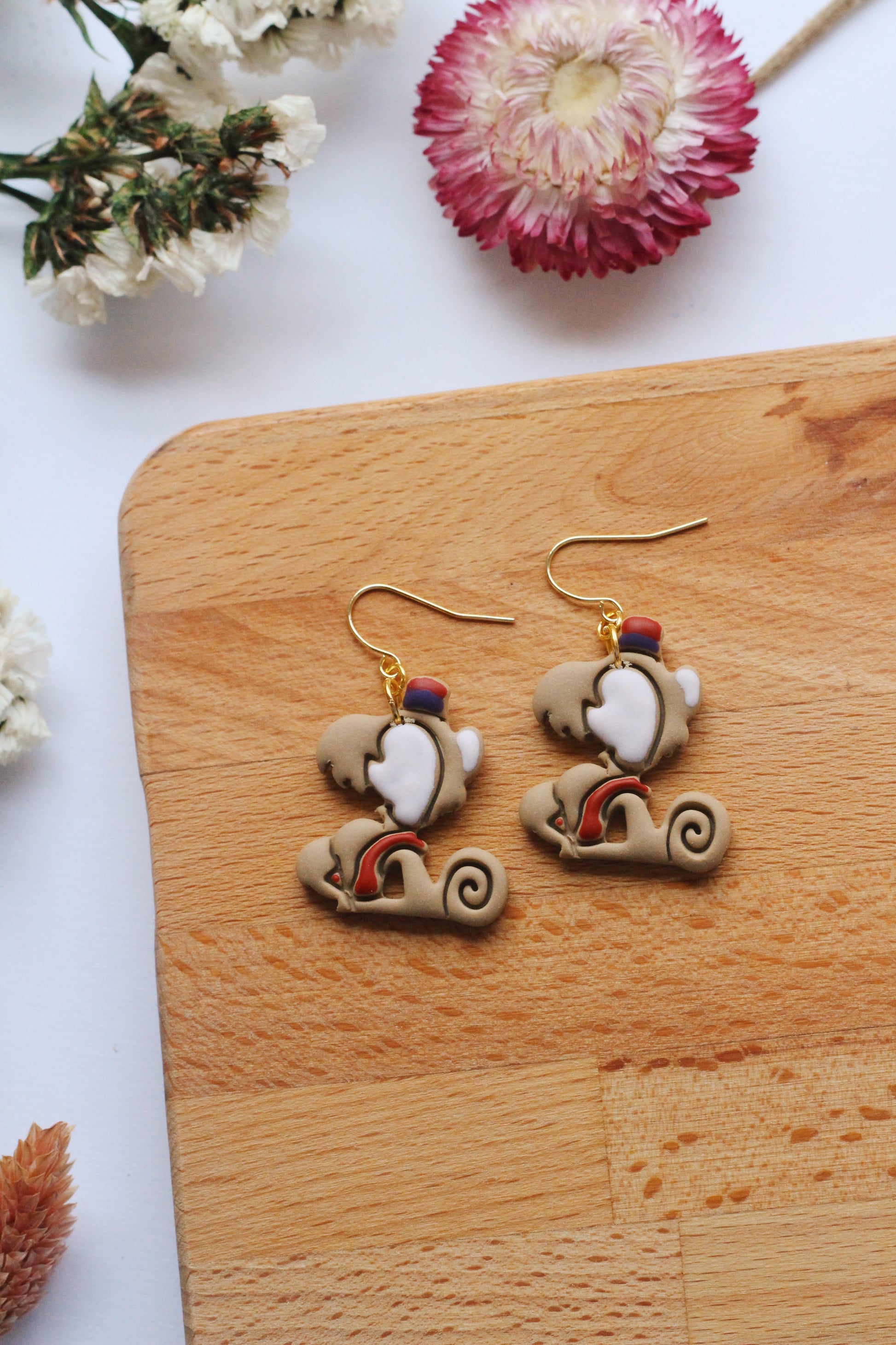 Pair of monkey  earrings on a wooden board with flowers in the background