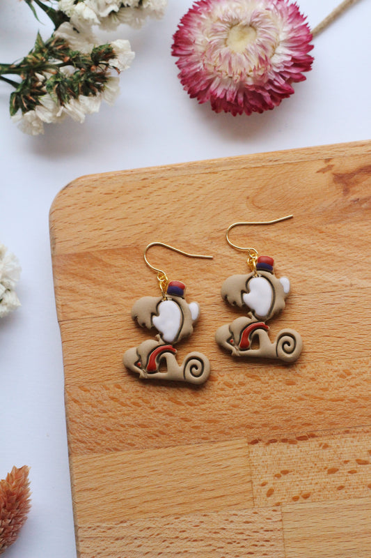 Pair of monkey  earrings on a wooden board with flowers in the background