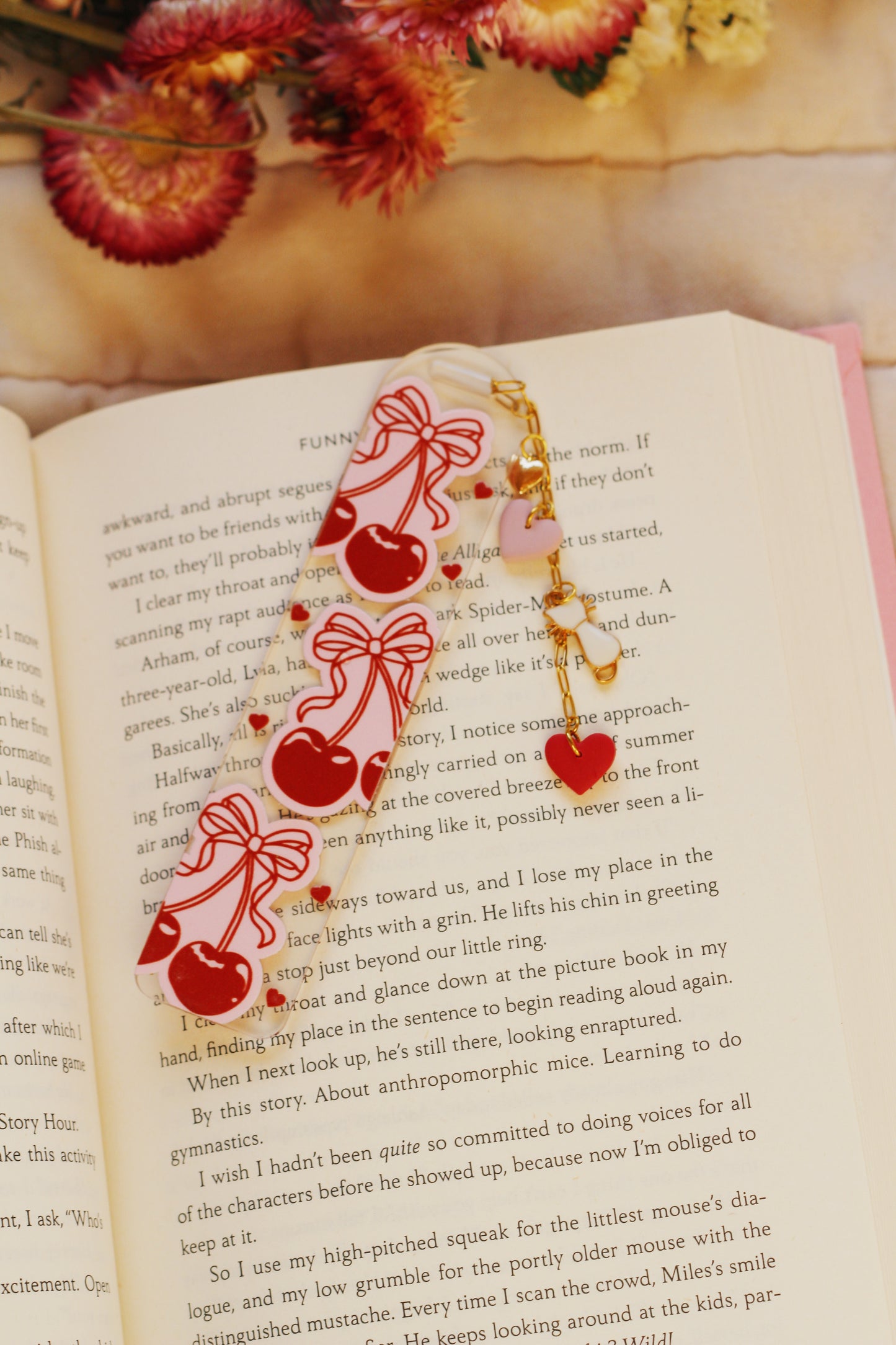 Decorative bookmarks with red hearts and ribbons on an open book with flowers in the background.