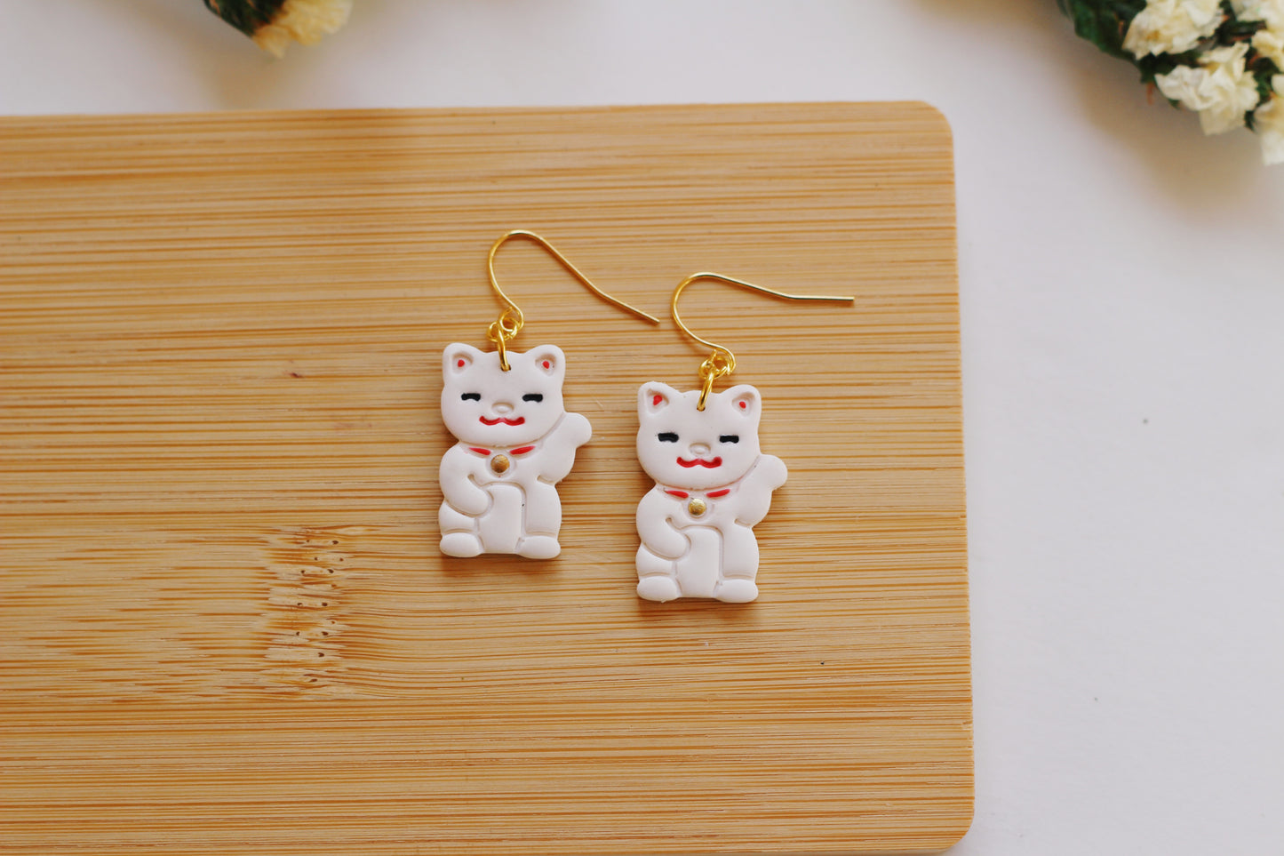 White cat statue earrings on a wooden board with a white background
