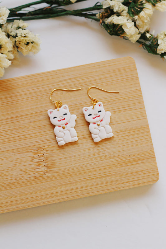 Pair of cat statue earrings, on a wooden surface with flowers in the background