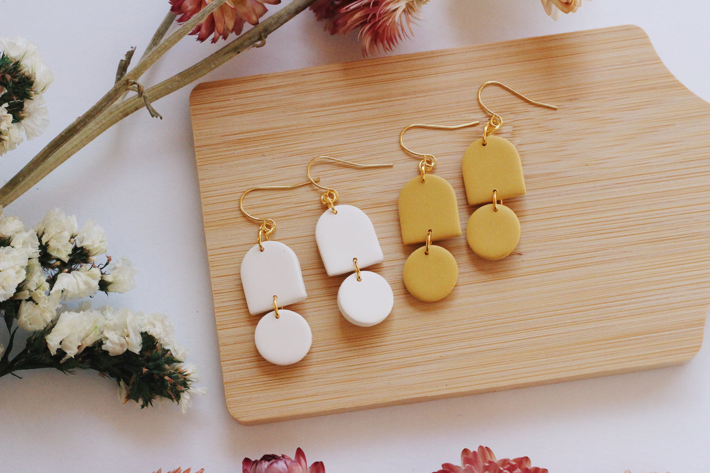 Yellow and white earrings on a wooden board with flowers in the background
