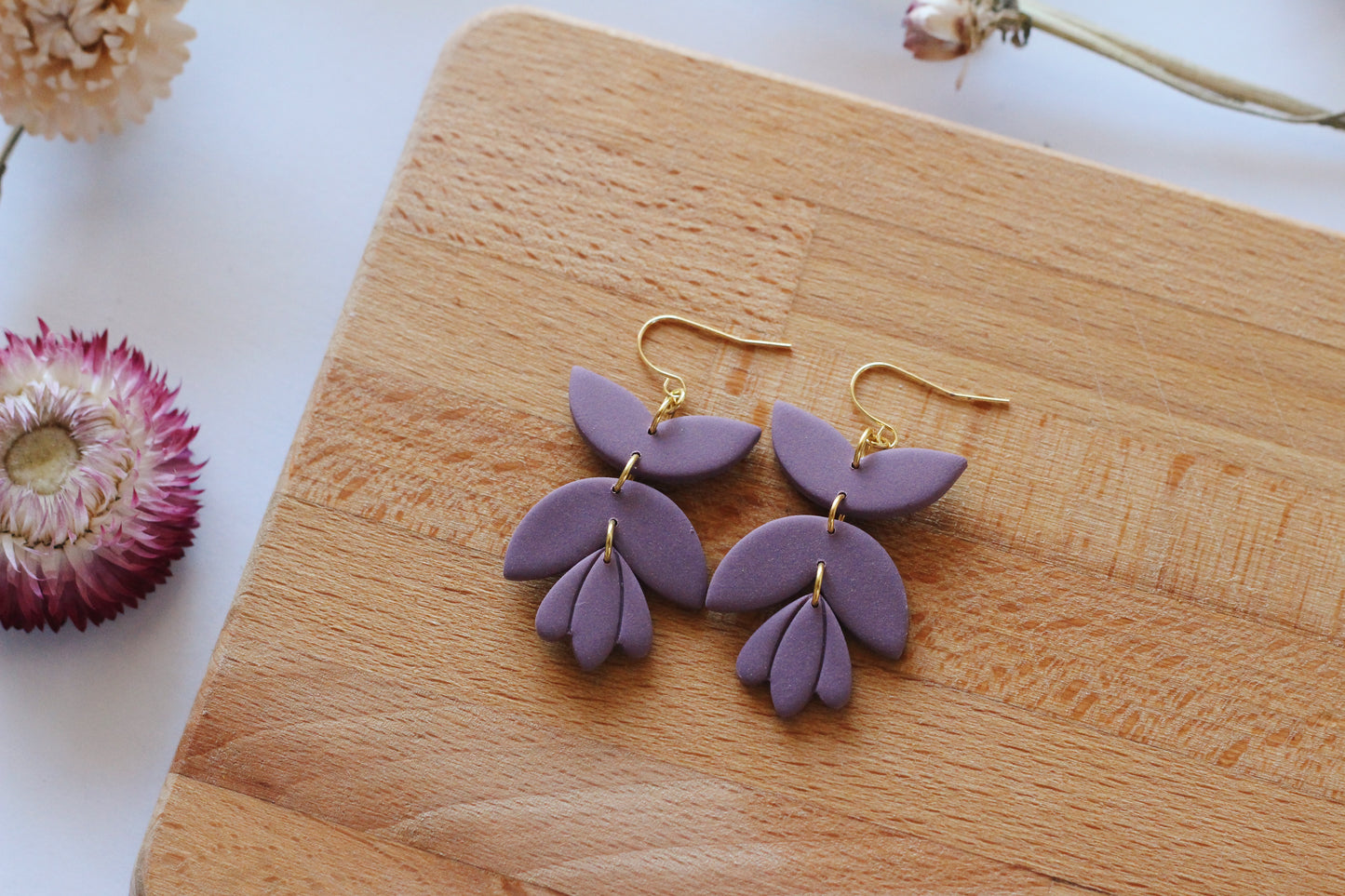Purple leaf-shaped earrings on a wooden surface with flowers in the background
