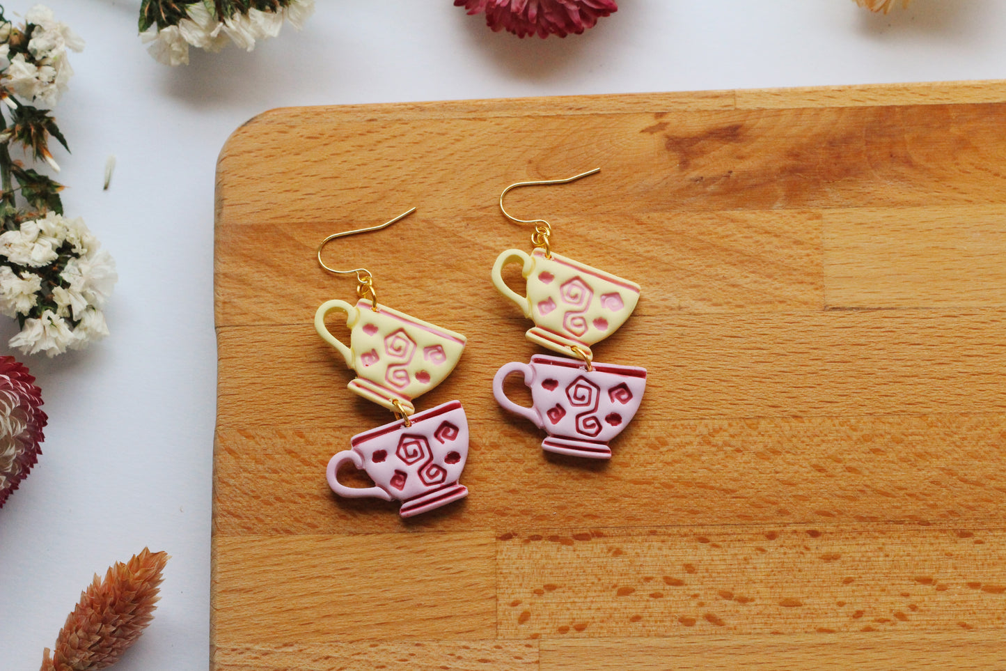 Teacup-shaped earrings on a wooden board with flowers around