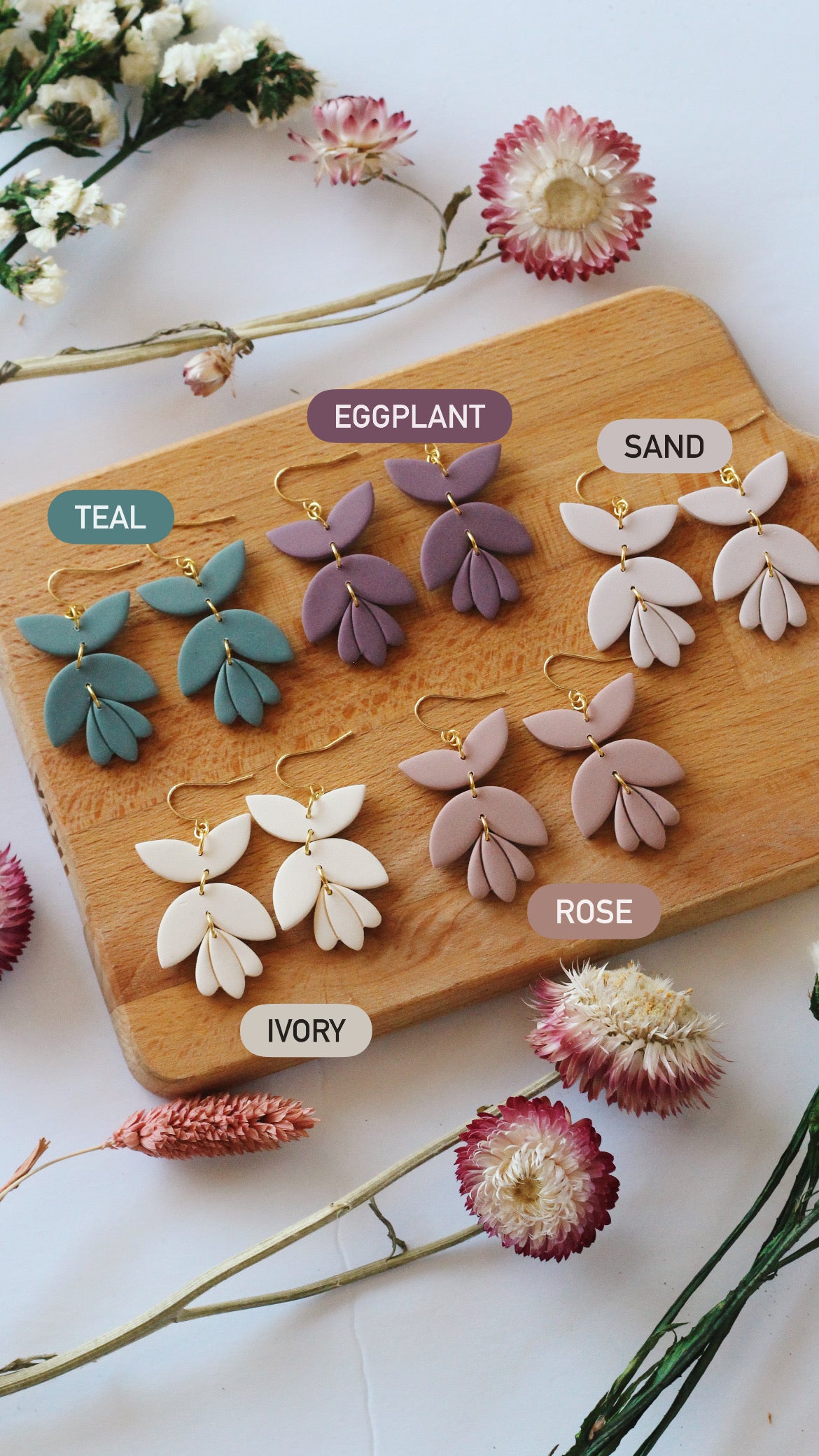 Set of floral earrings on a wooden board with color labels surrounded by flowers.