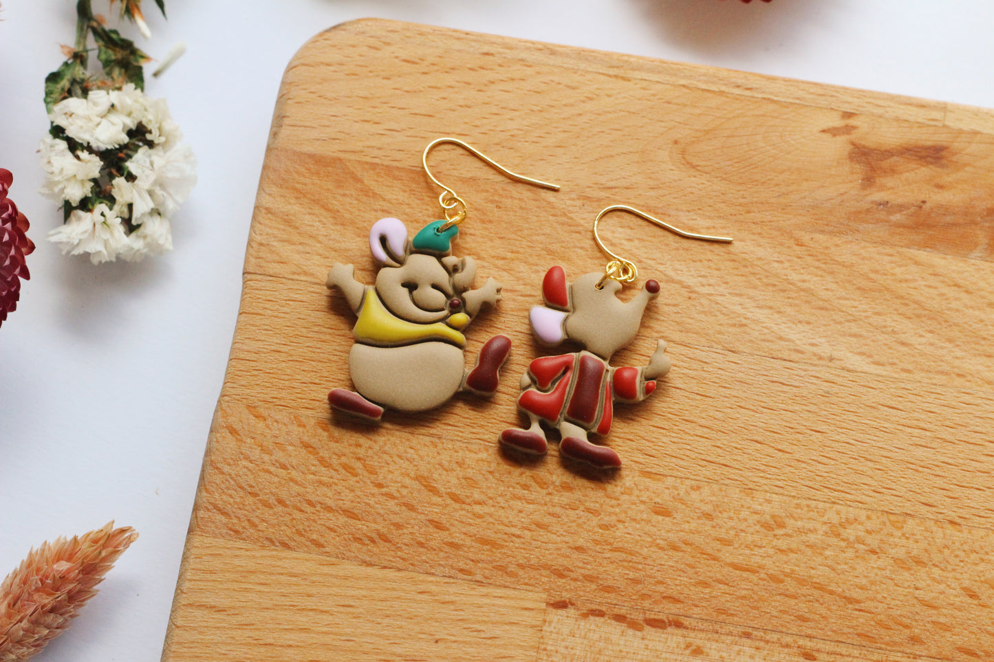 Cartoon character earrings on a wooden board with flowers in the background