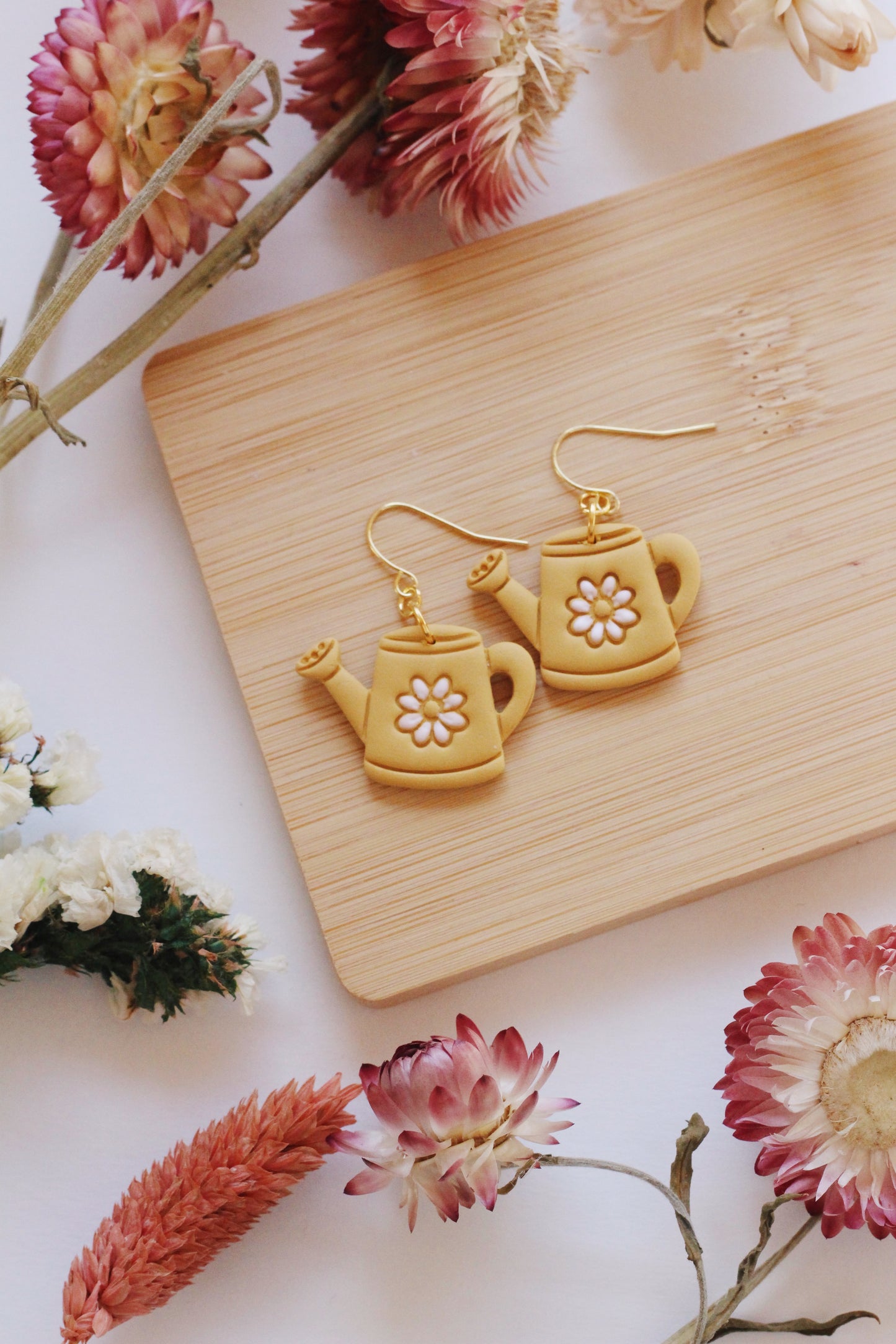 Teapot-shaped earrings on a wooden board with flowers around