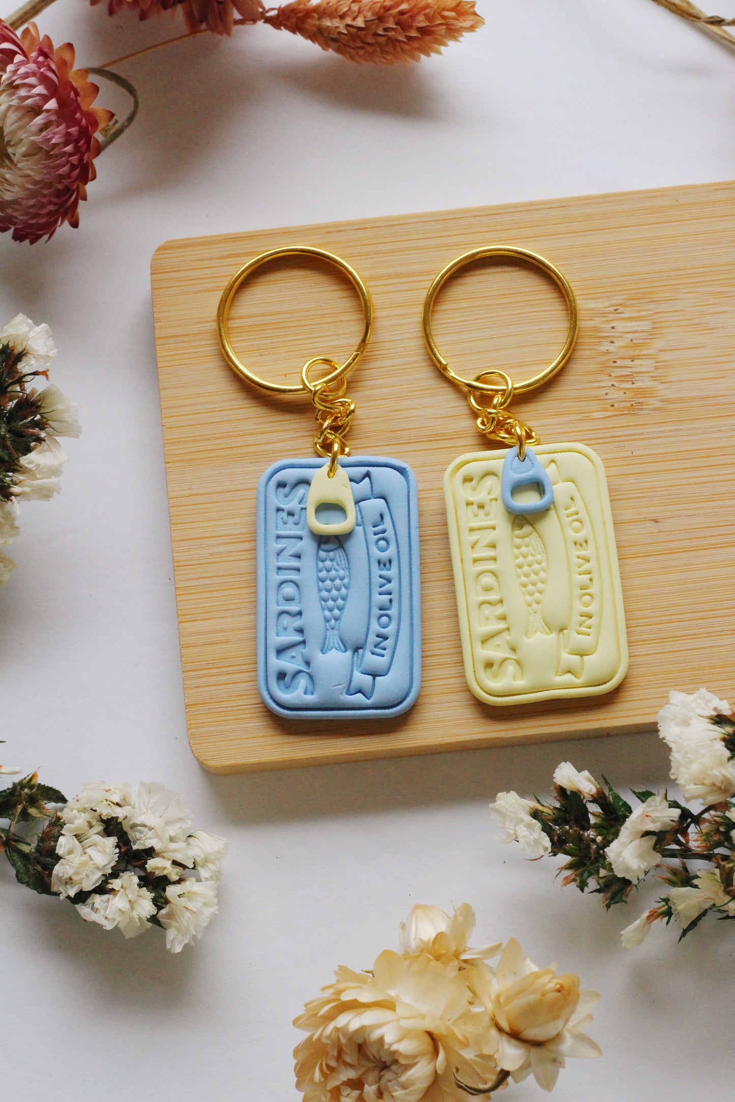 Two keychains on a wooden block with dried flowers around