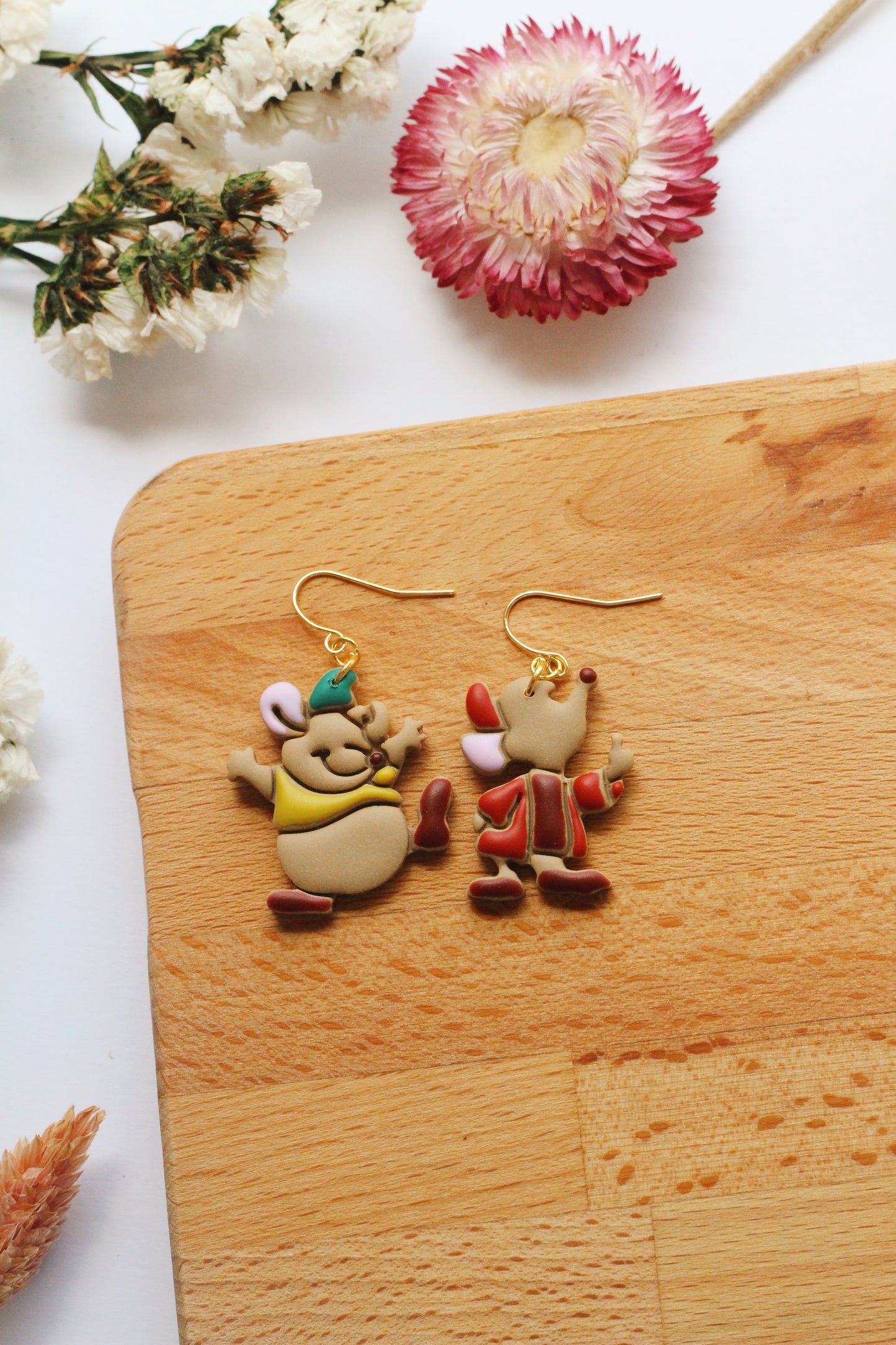 Two cartoon character mice earrings on a wooden board with flowers in the background