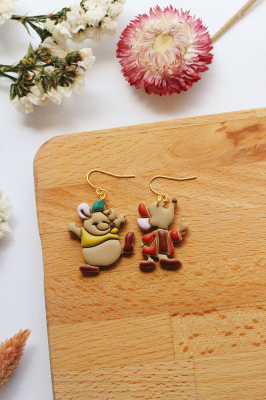 Two cartoon character mice earrings on a wooden board with flowers in the background