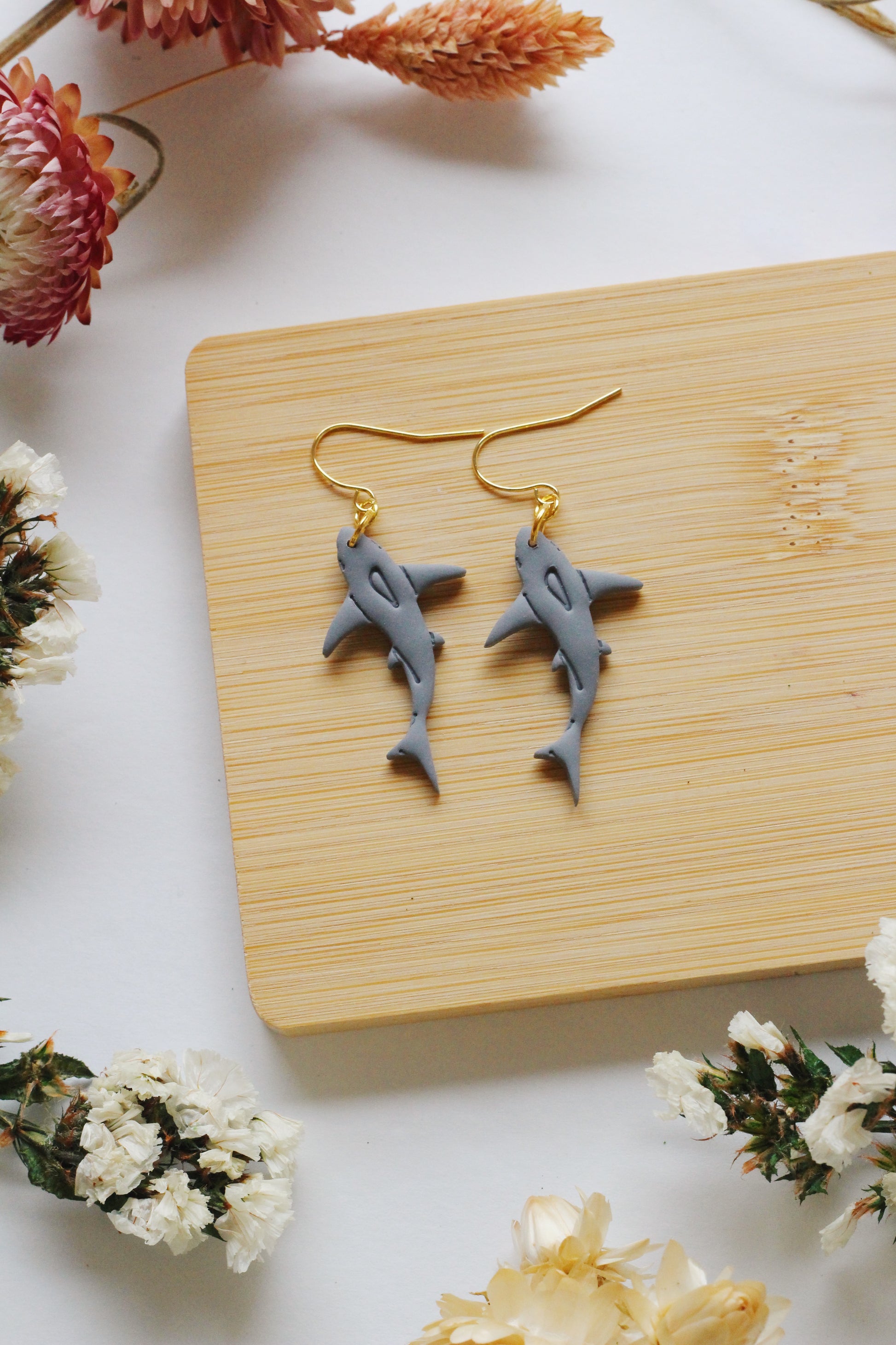 Shark-shaped earrings on a wooden board with flowers around