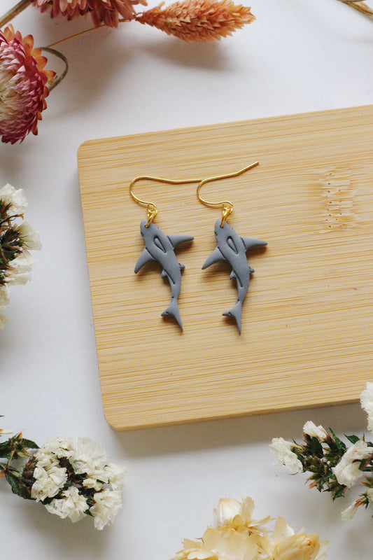Shark-shaped earrings on a wooden board with flowers around