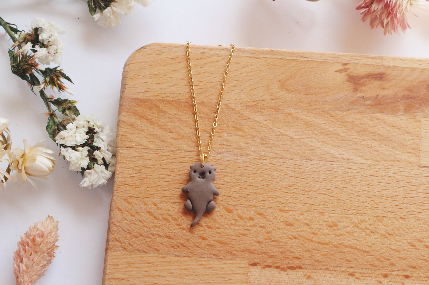 Necklace with an otter pendant on a wooden surface with flowers in the background
