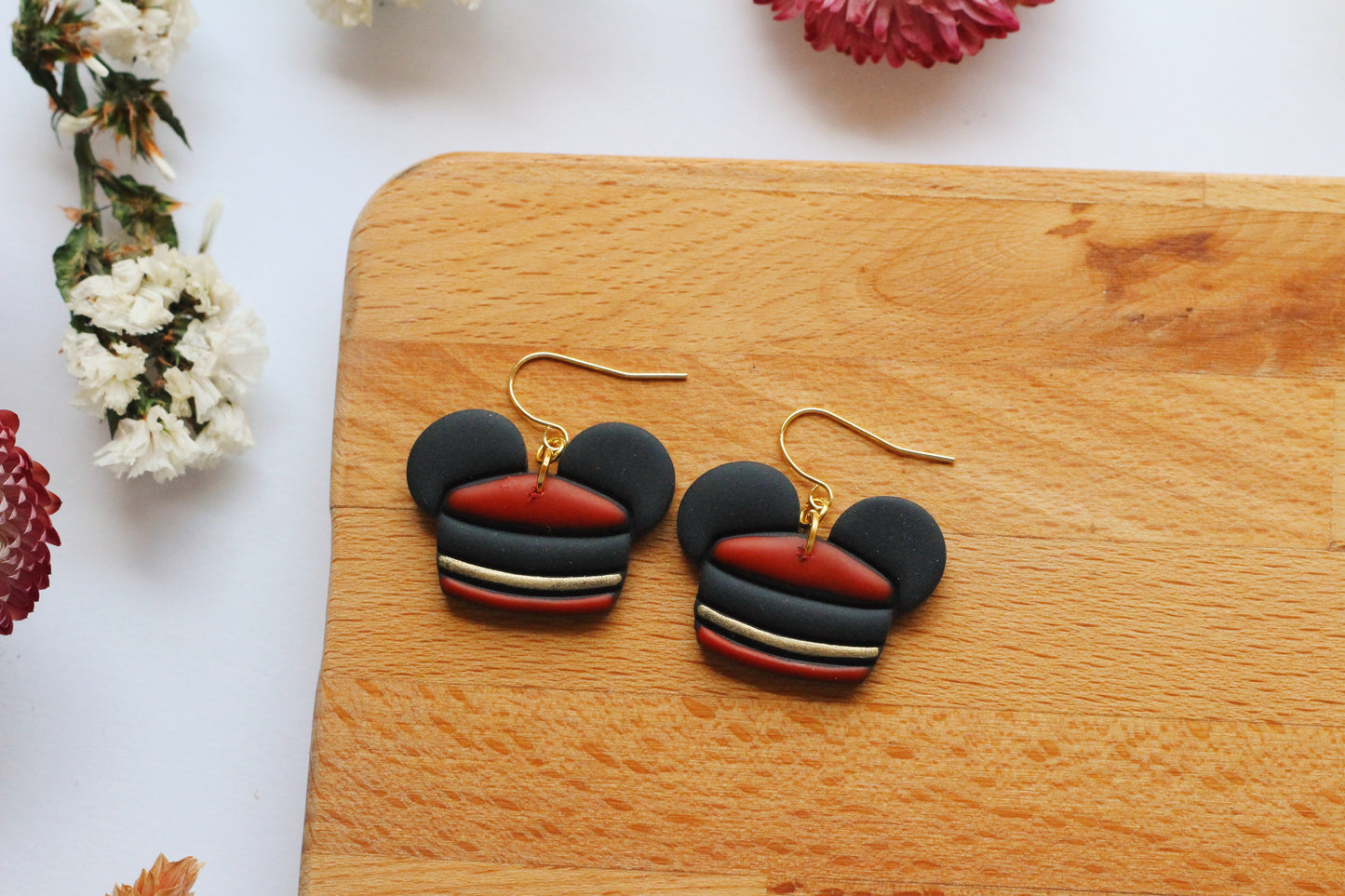 Black and red mouse earrings on a wooden board with flowers in the background