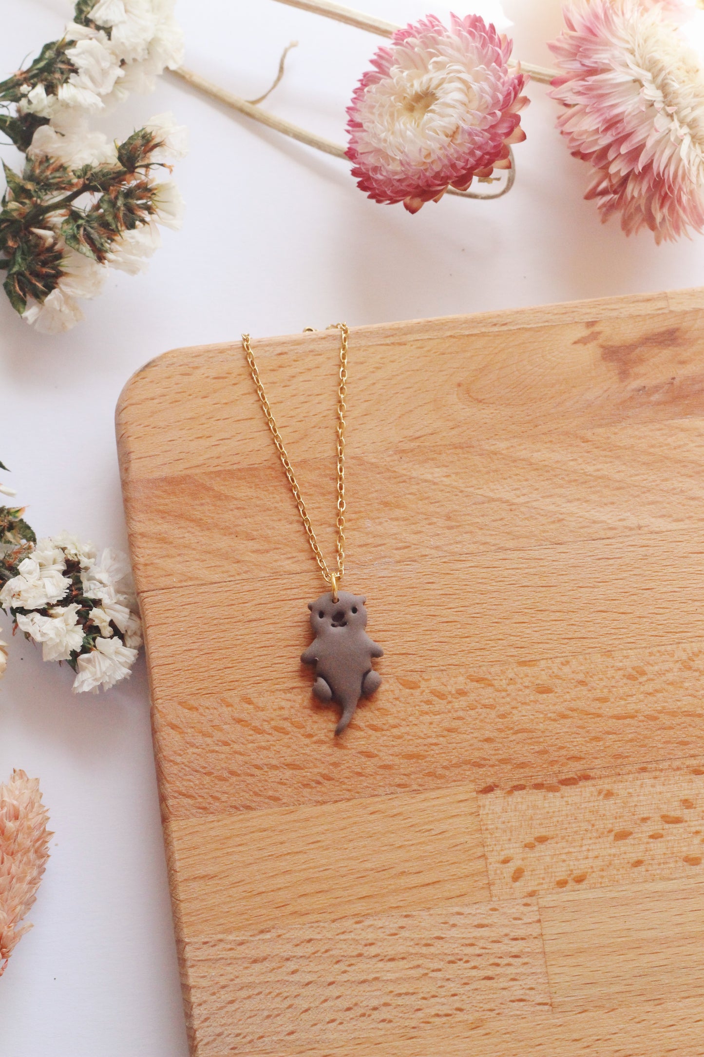 Necklace with an otter pendant on a wooden surface surrounded by flowers