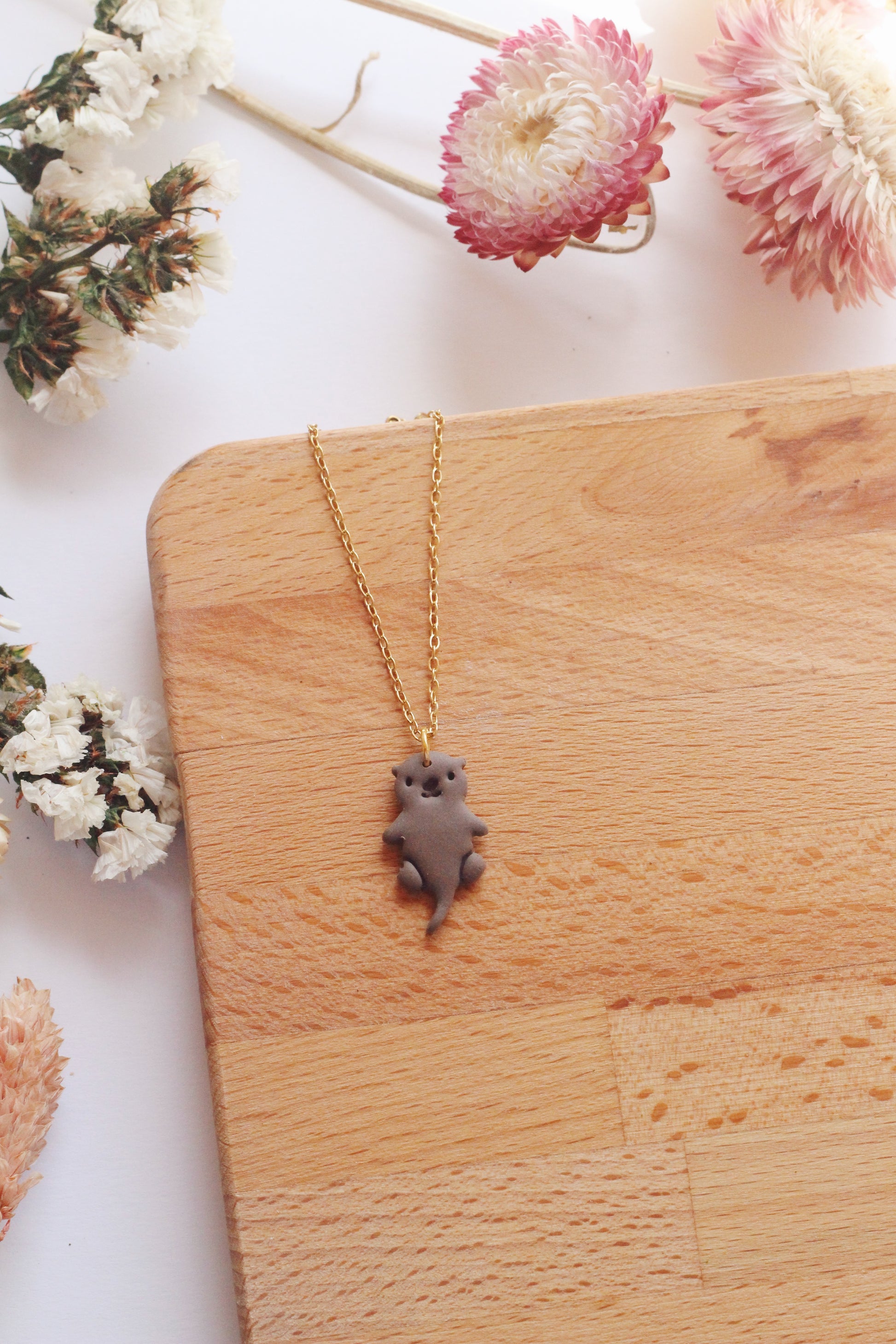 Necklace with an otter pendant on a wooden surface surrounded by flowers