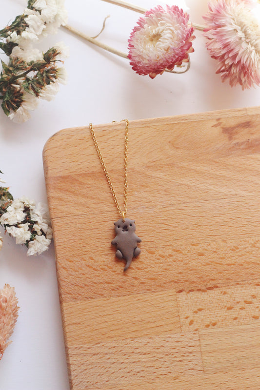 Necklace with an otter pendant on a wooden surface surrounded by flowers