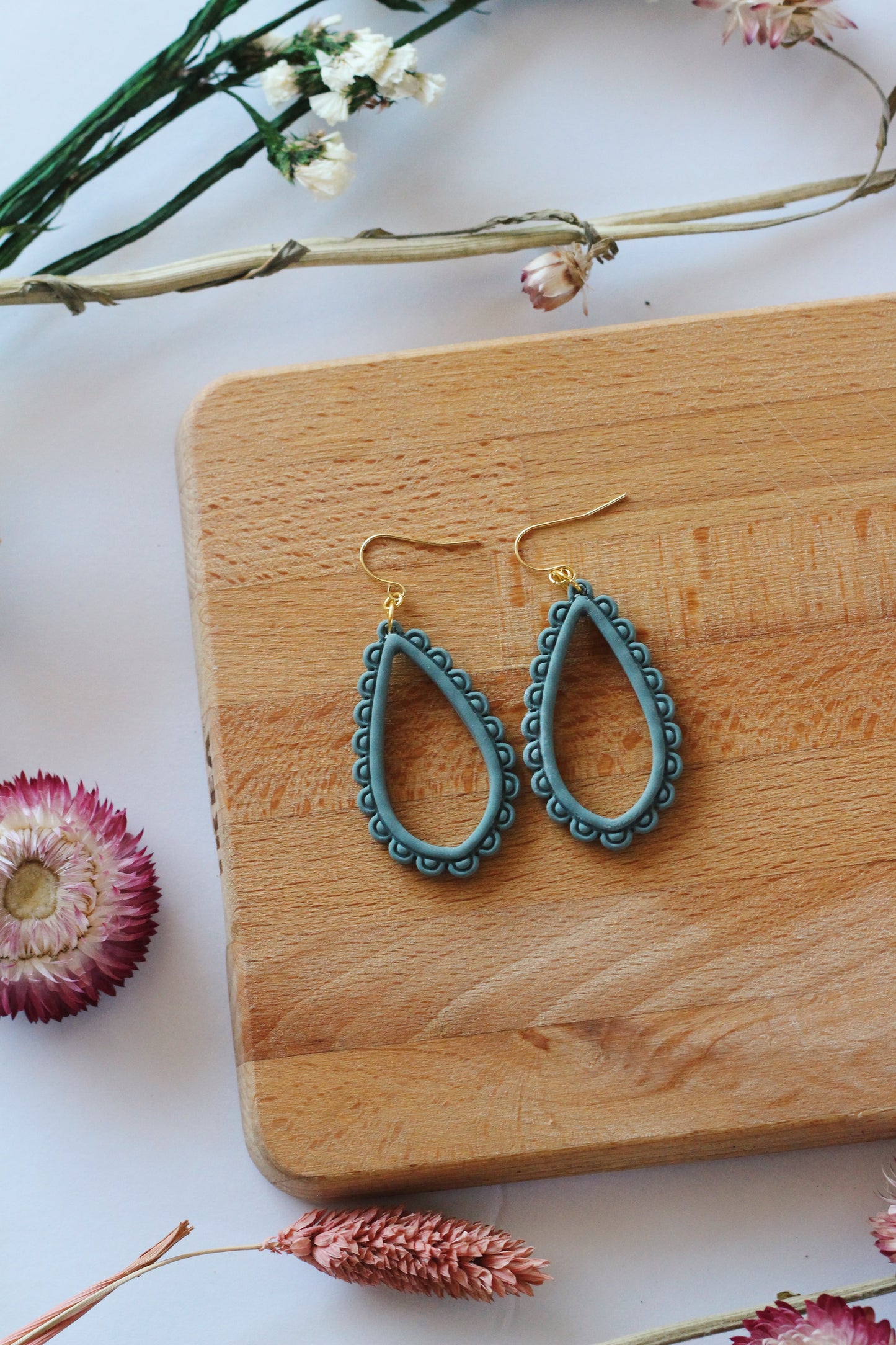 Teal earrings on a wooden board with flowers around