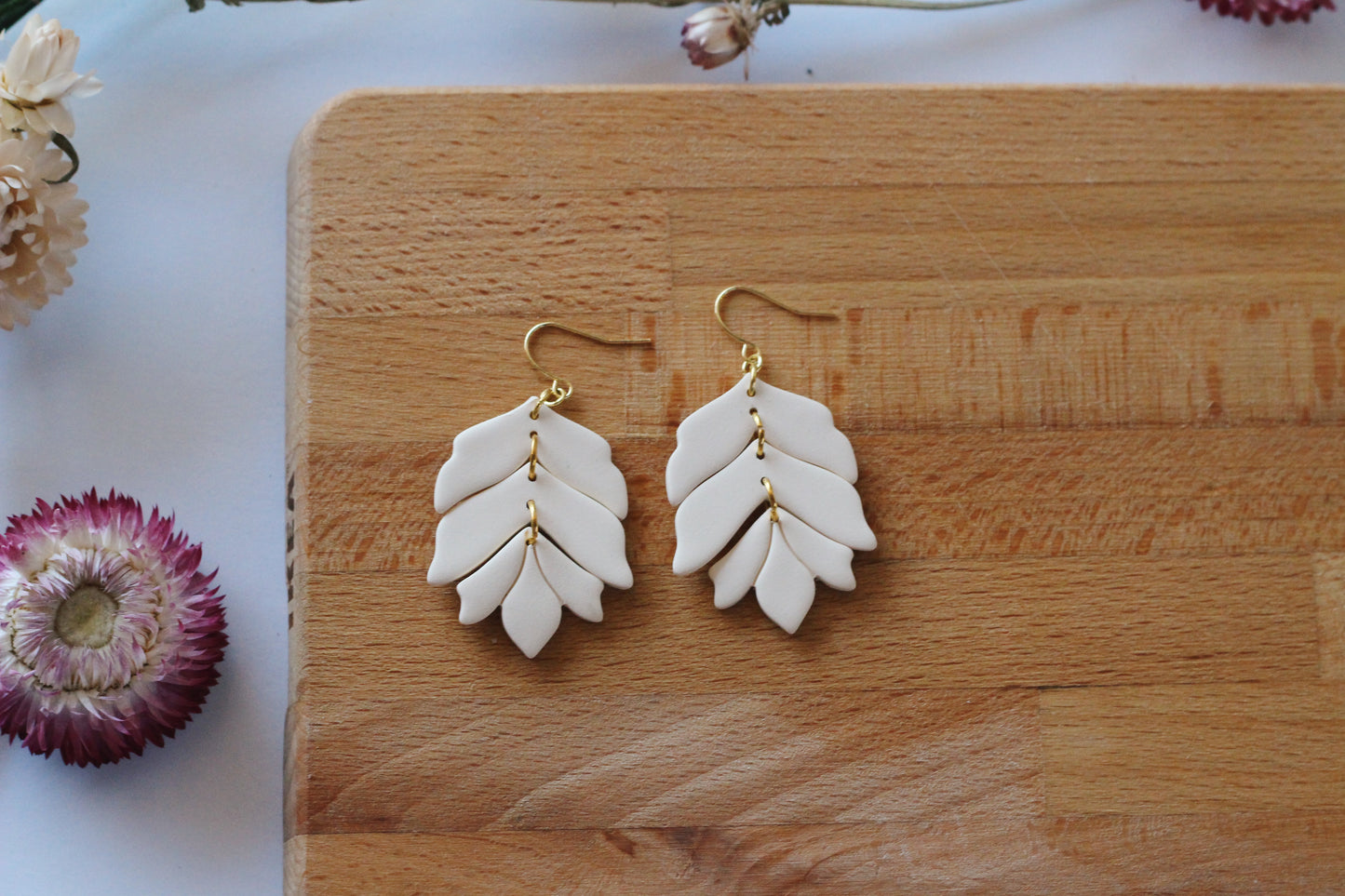 White leaf-shaped earrings with gold accents on a wooden surface.