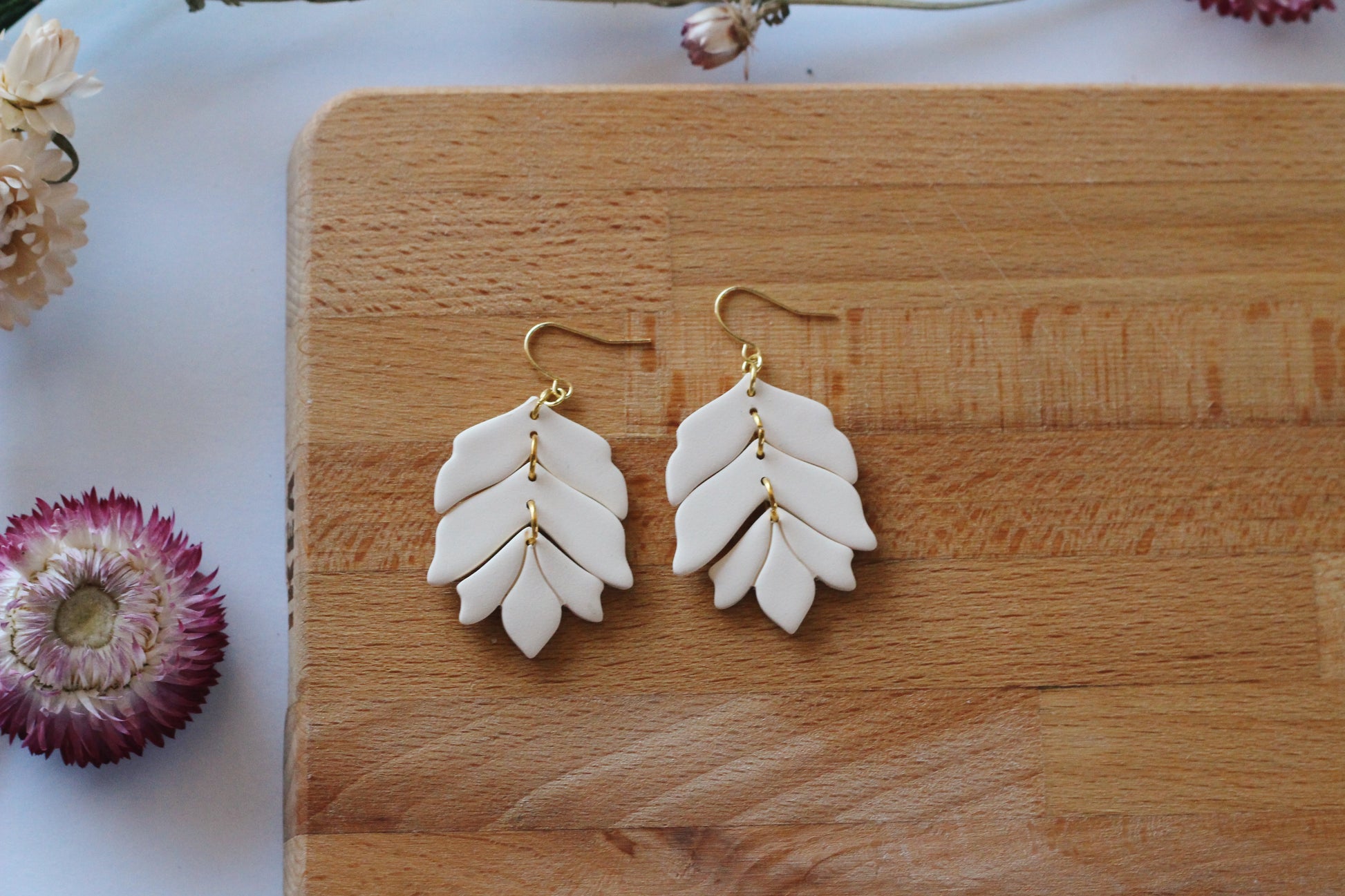 White leaf-shaped earrings with gold accents on a wooden surface.
