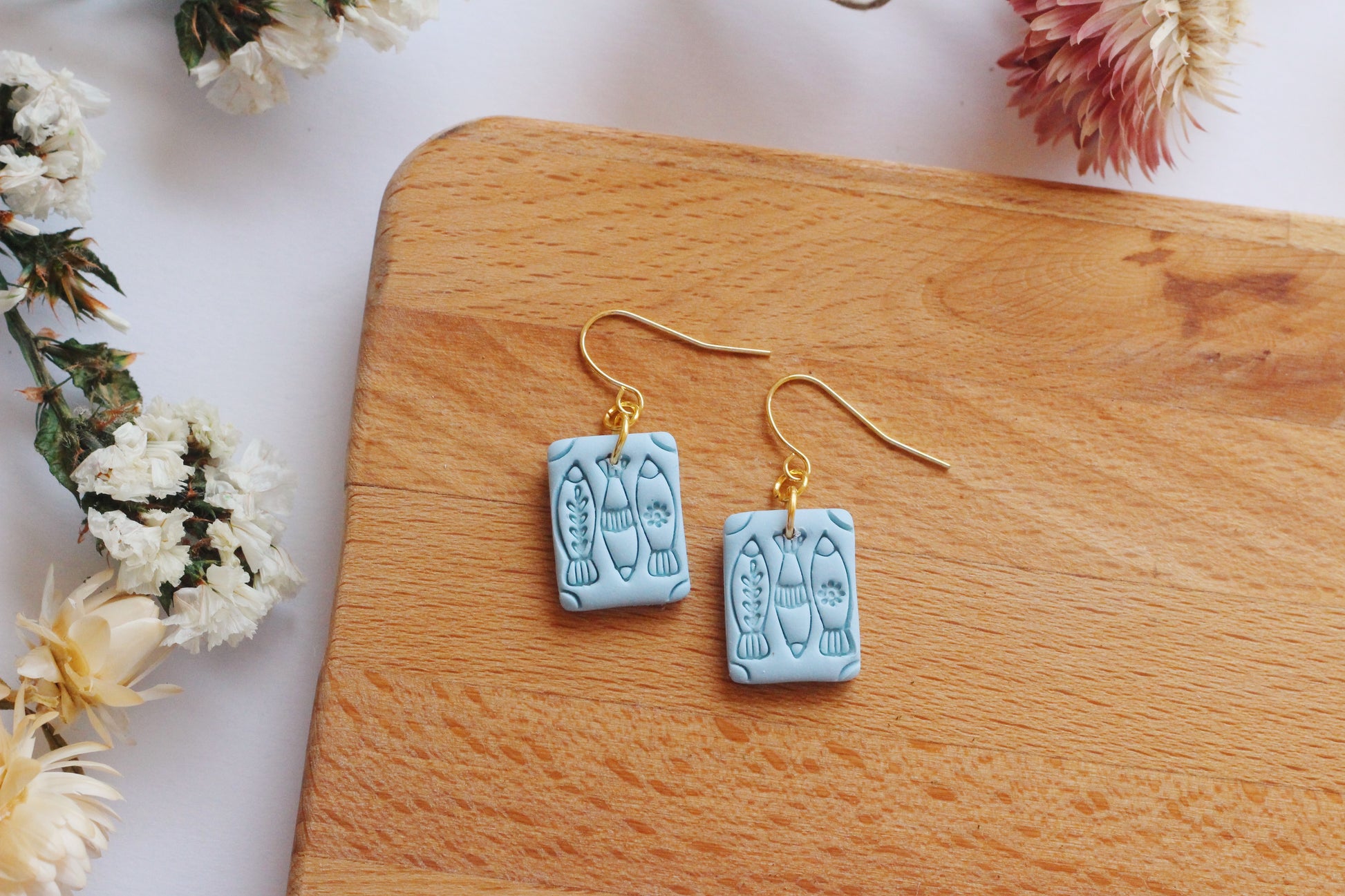 Blue earrings with gold hooks on a wooden surface surrounded by flowers