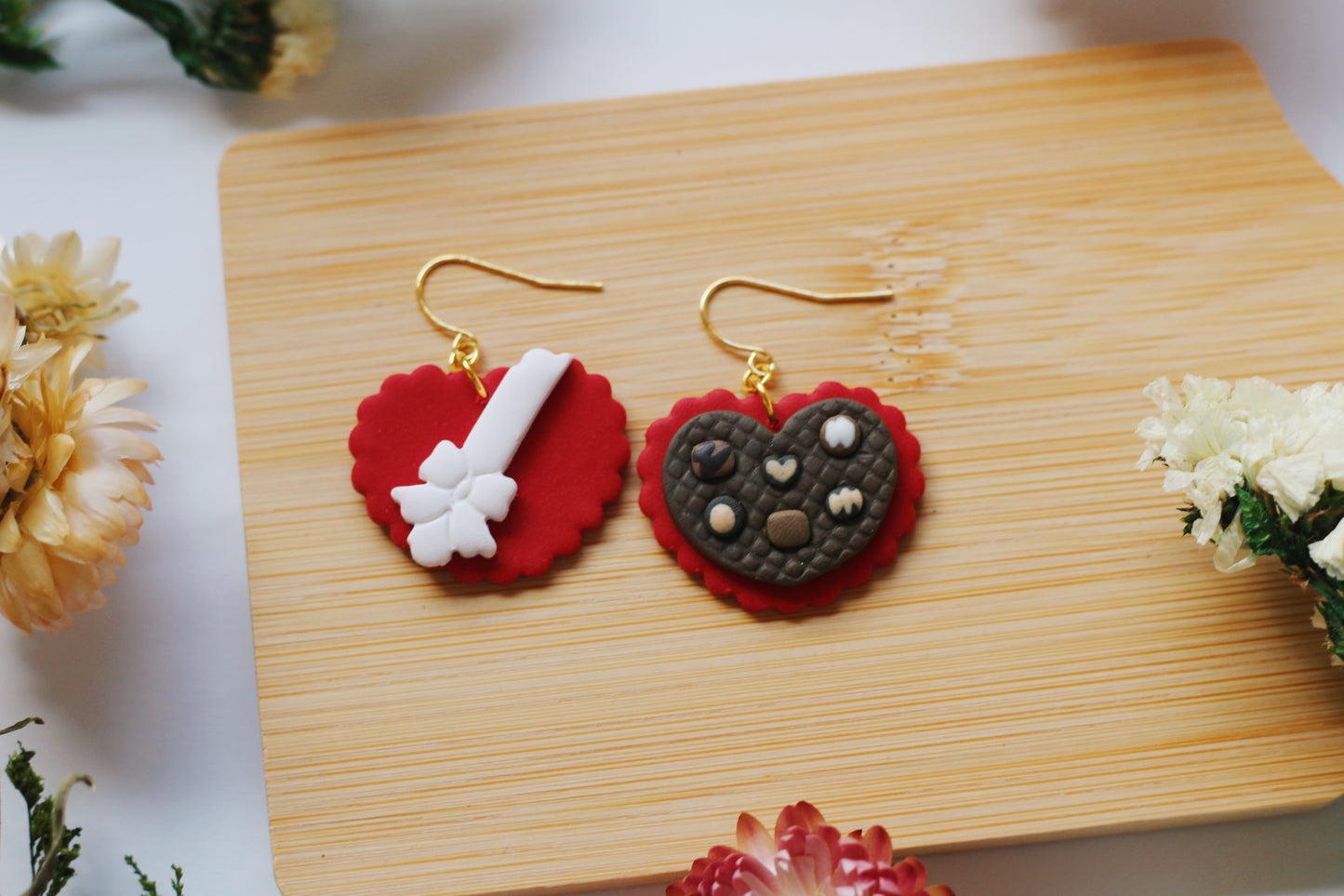 Heart-shaped chocolate box earrings on a wooden board with flowers around