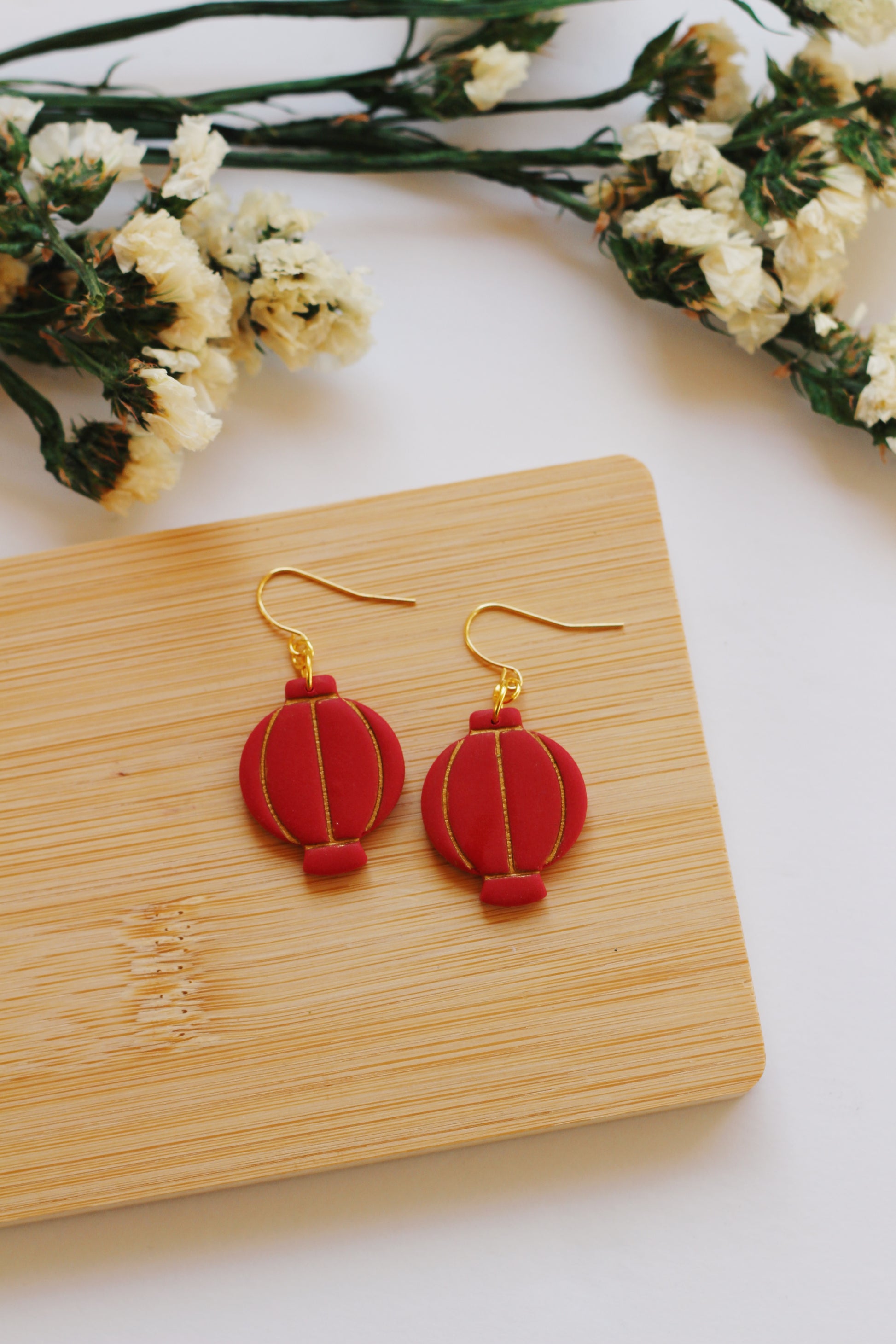 Red lantern-shaped earrings on a wooden board with flowers in the background
