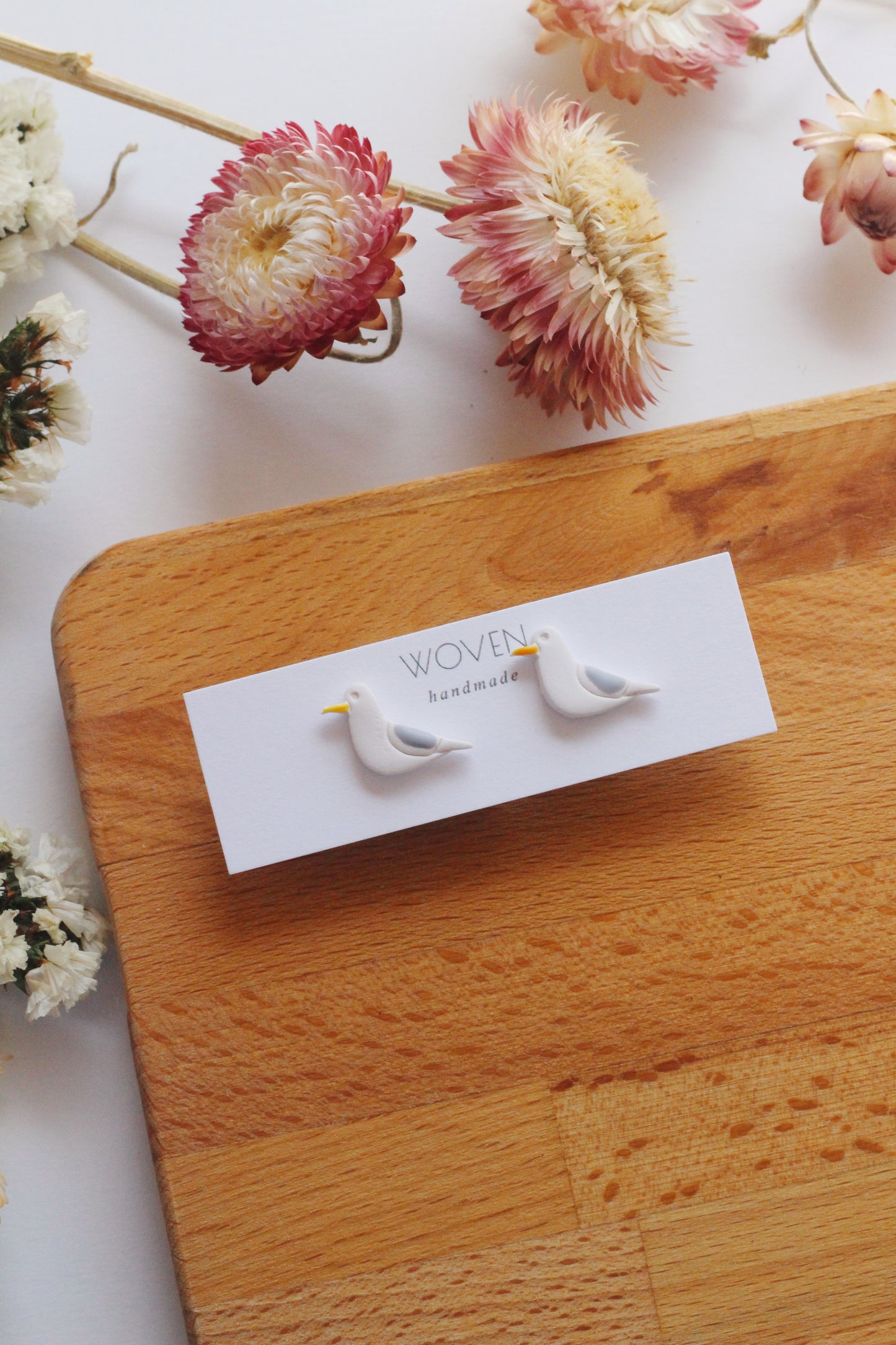 Seagull earrings on a white card with flowers in the background