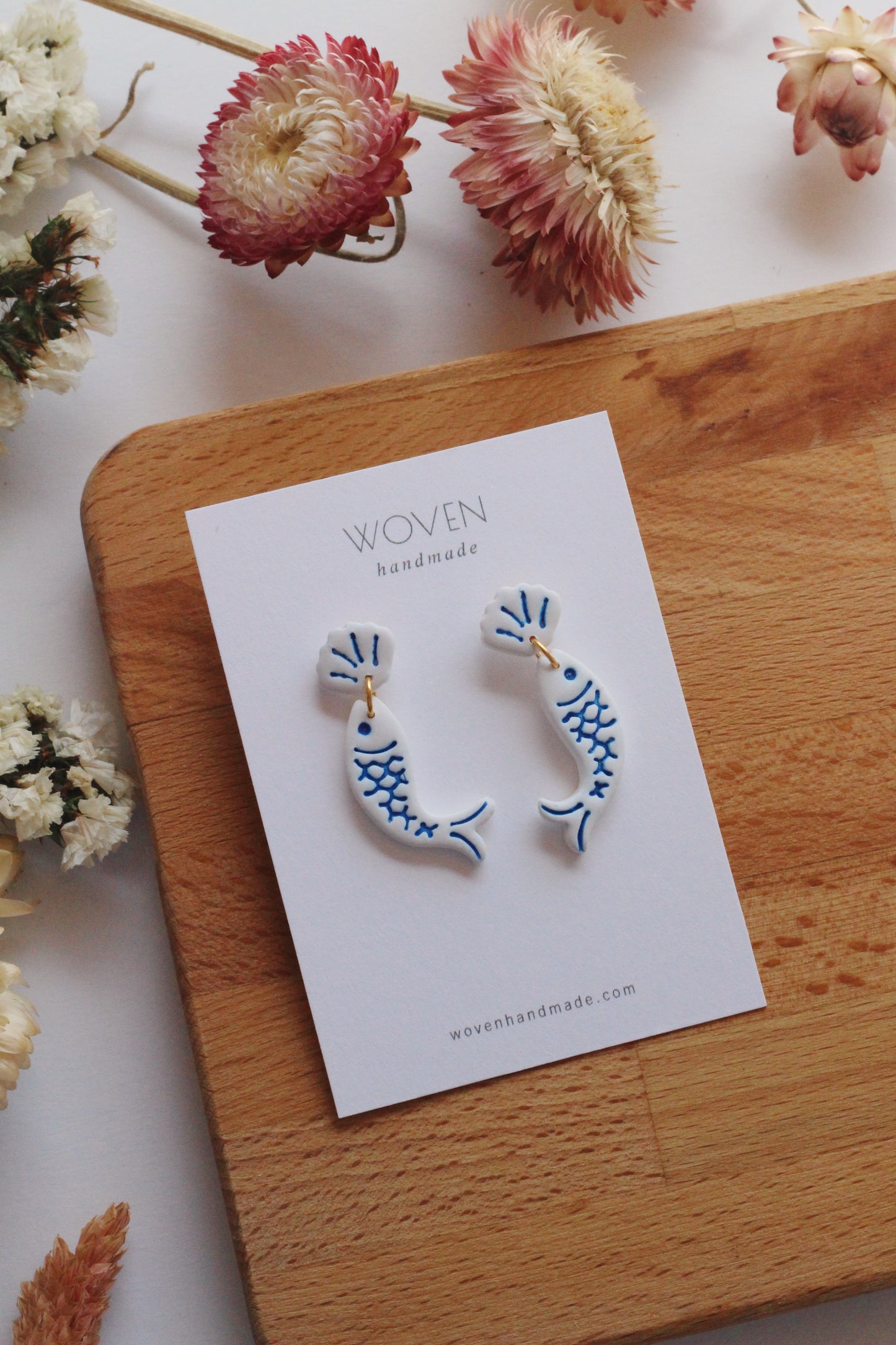 Pair of fish-shaped earrings on a 'Woven Handmade' card with flowers around