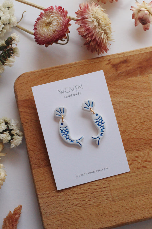 Pair of fish-shaped earrings on a 'Woven Handmade' card with flowers around