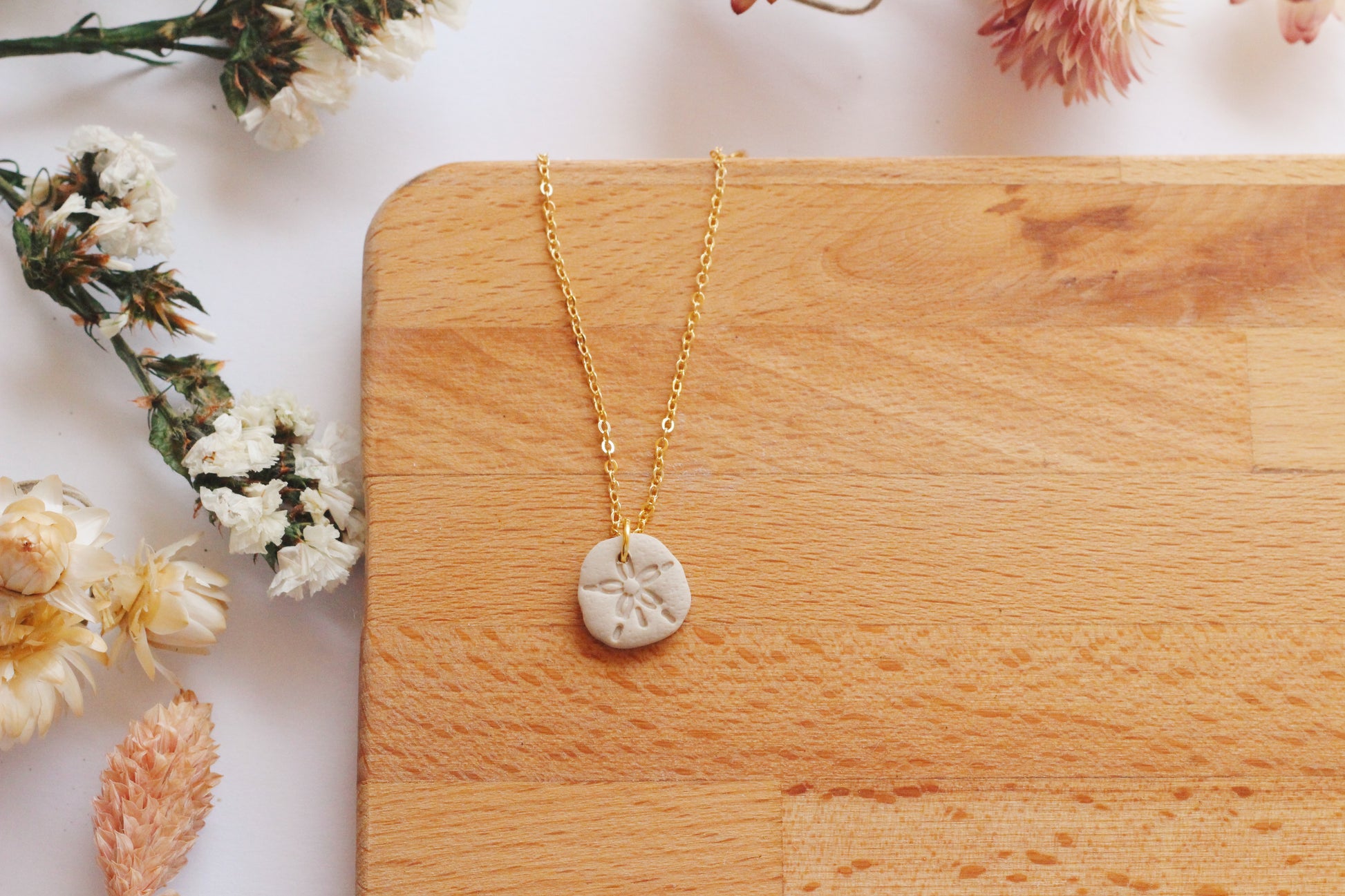 Gold necklace with a sand dollar pendant on a wooden surface surrounded by flowers