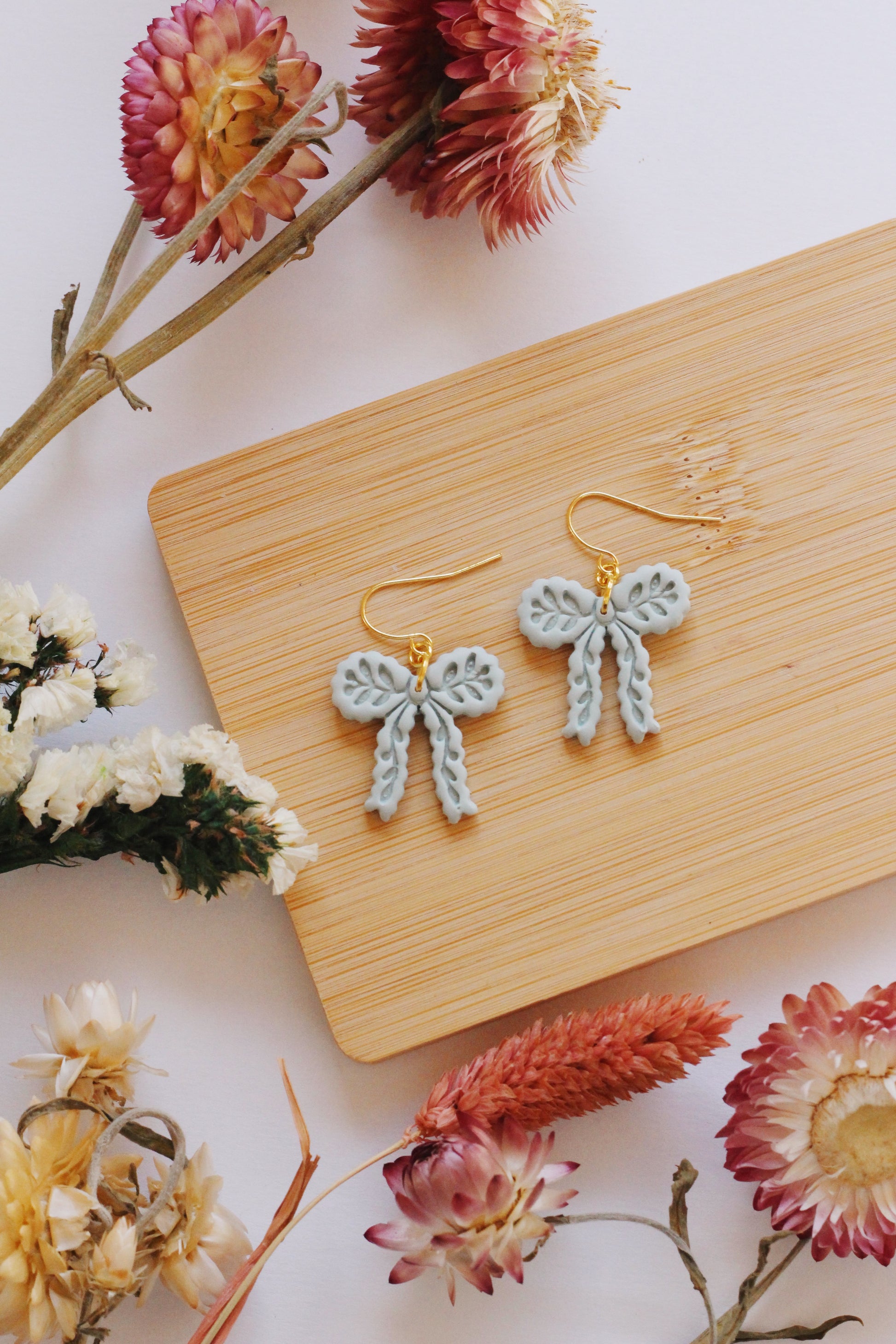 Bow-shaped earrings on a wooden board with flowers around