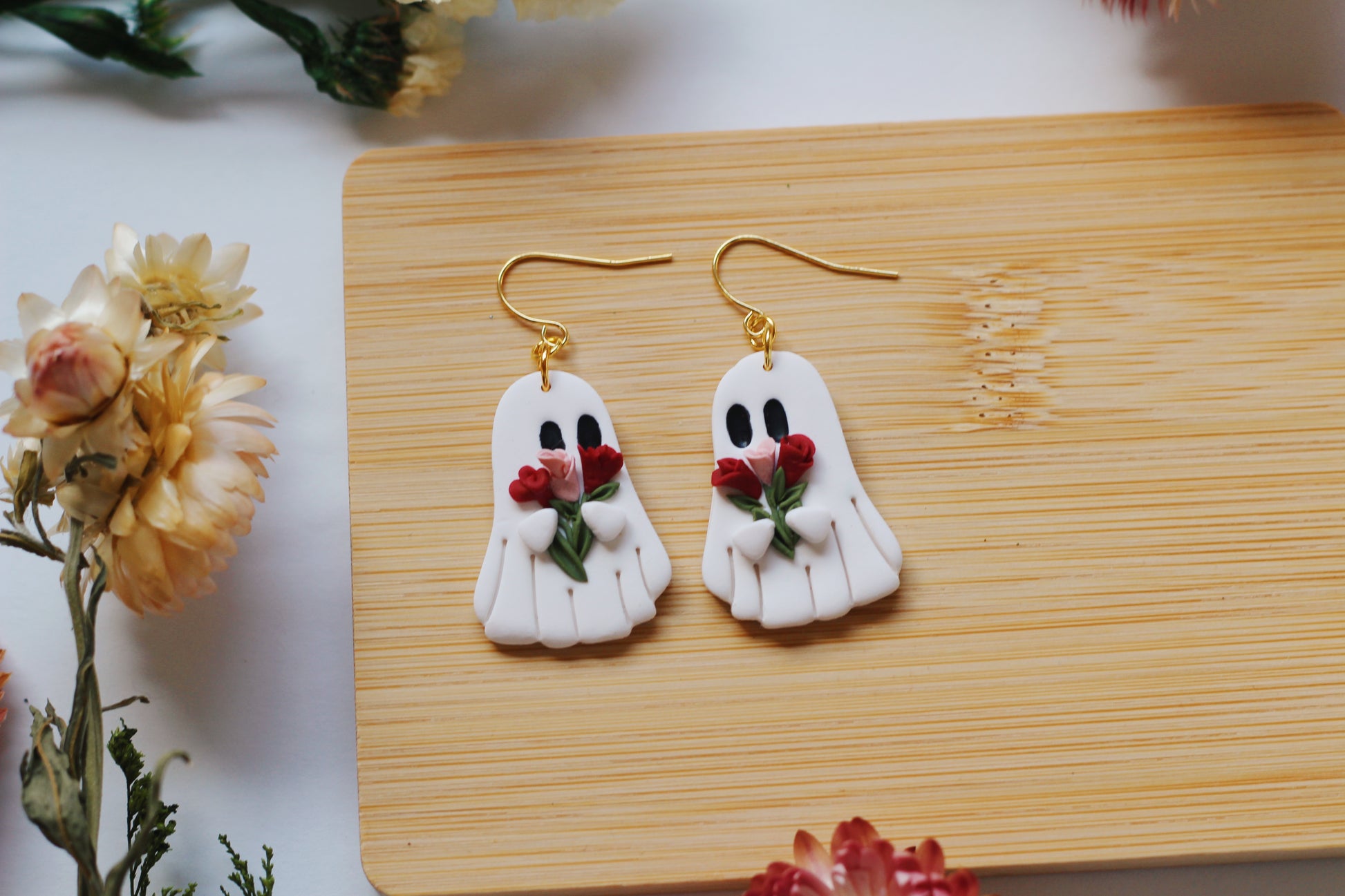 Ghost-shaped earrings with a bouquet of flowers on a wooden board with flowers around