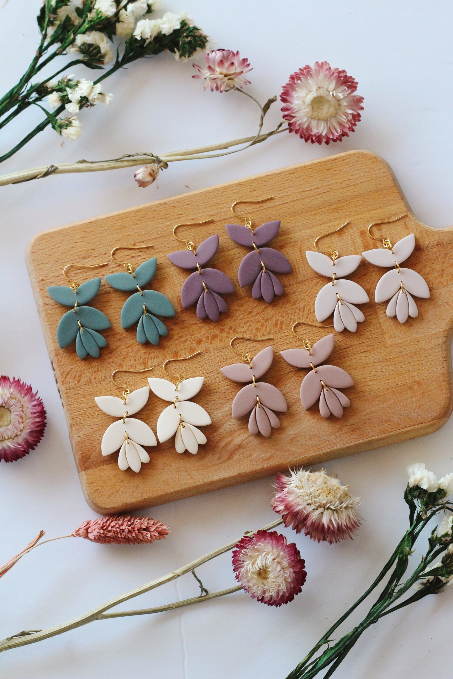 Set of floral-themed earrings on a wooden display board with flowers around.